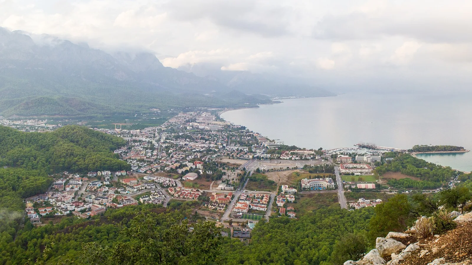 Dağlarla çevrili Akdeniz kıyı kasabası, yeşil orman ve mavi deniz manzarası