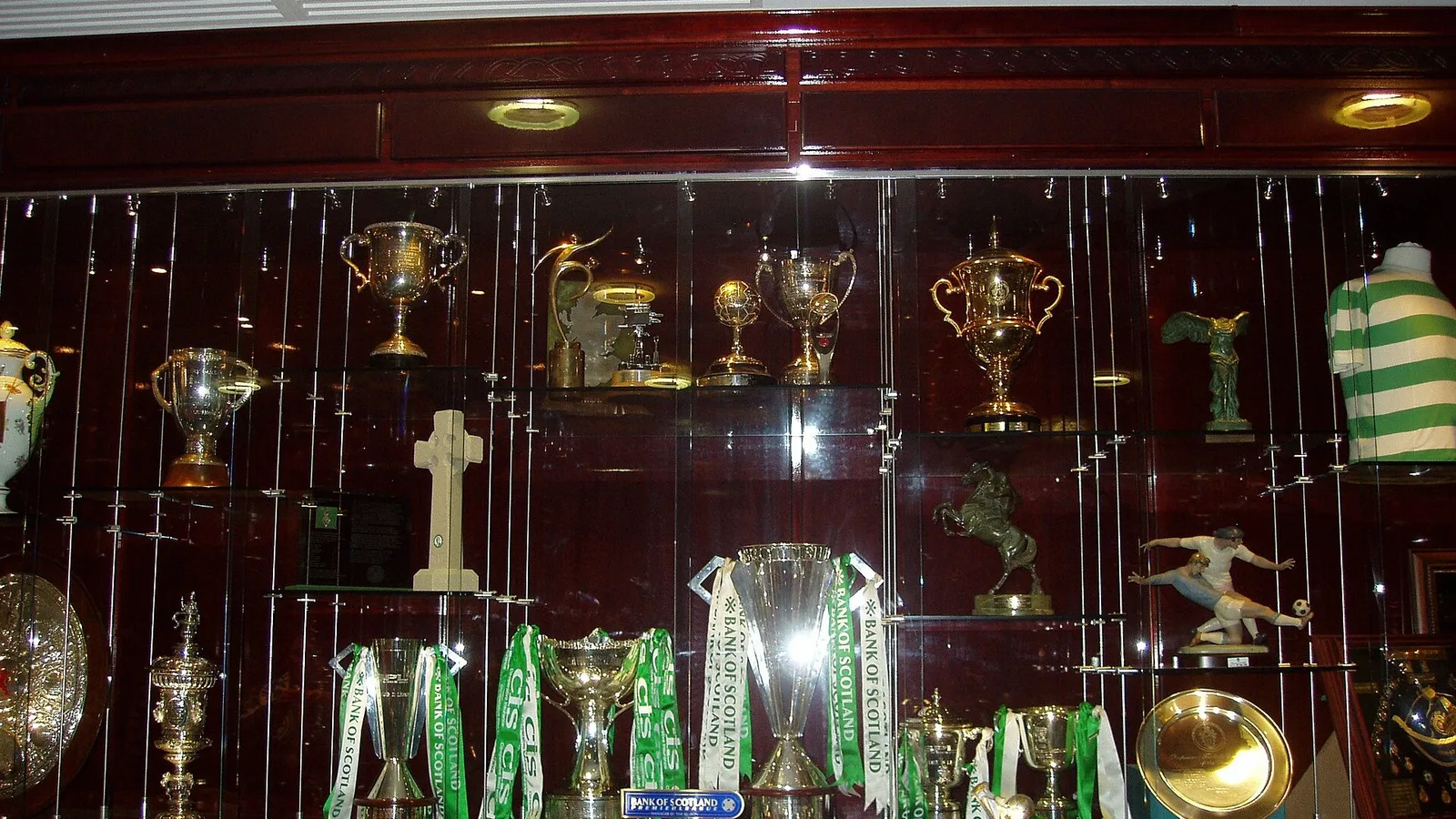 Futbol kupasıyla dolu kapalı cam vitrin, çeşitli altın ve gümüş şekilli kupalar ve troféler sergileniyor.