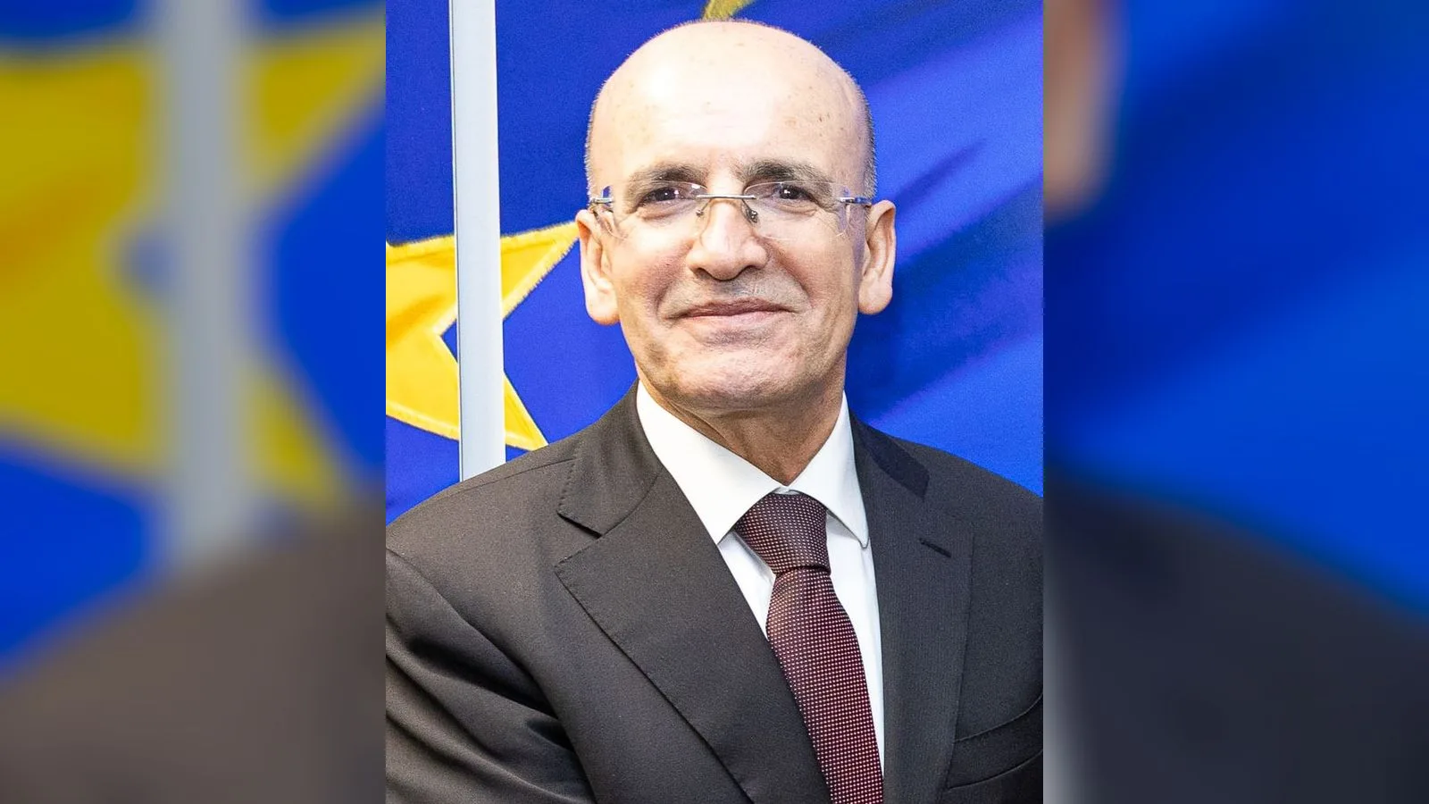 Gözlüklü, yakın dönem bir siyasi figürün portresi resmi arka plana karşı.