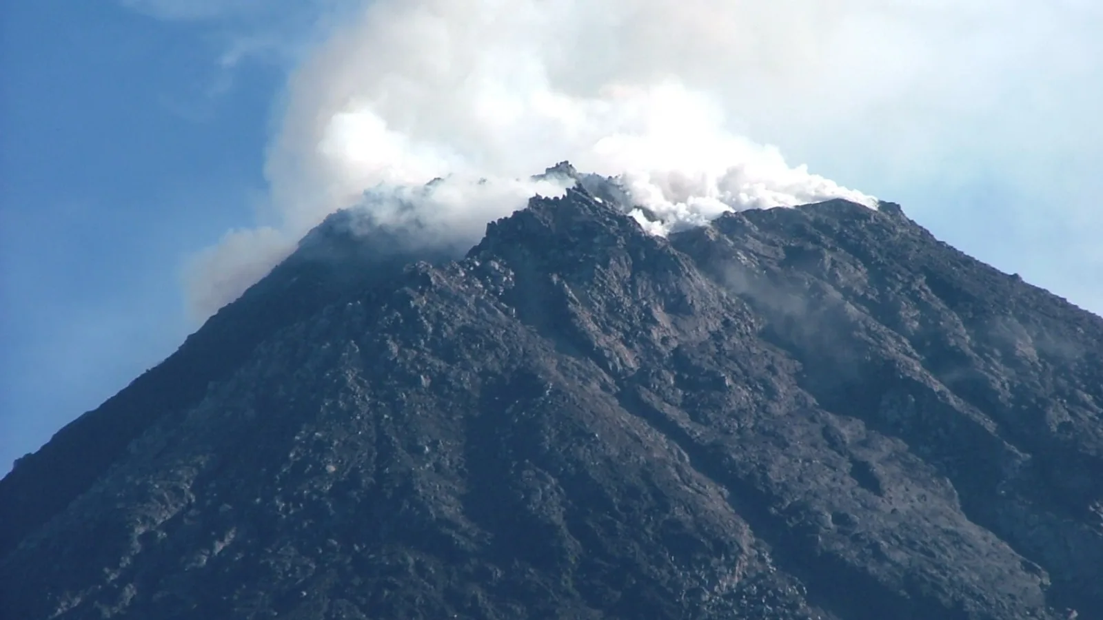 Beyaz bulutlu dağ başı, koyu gri kayalı Merapi yanardağı.
