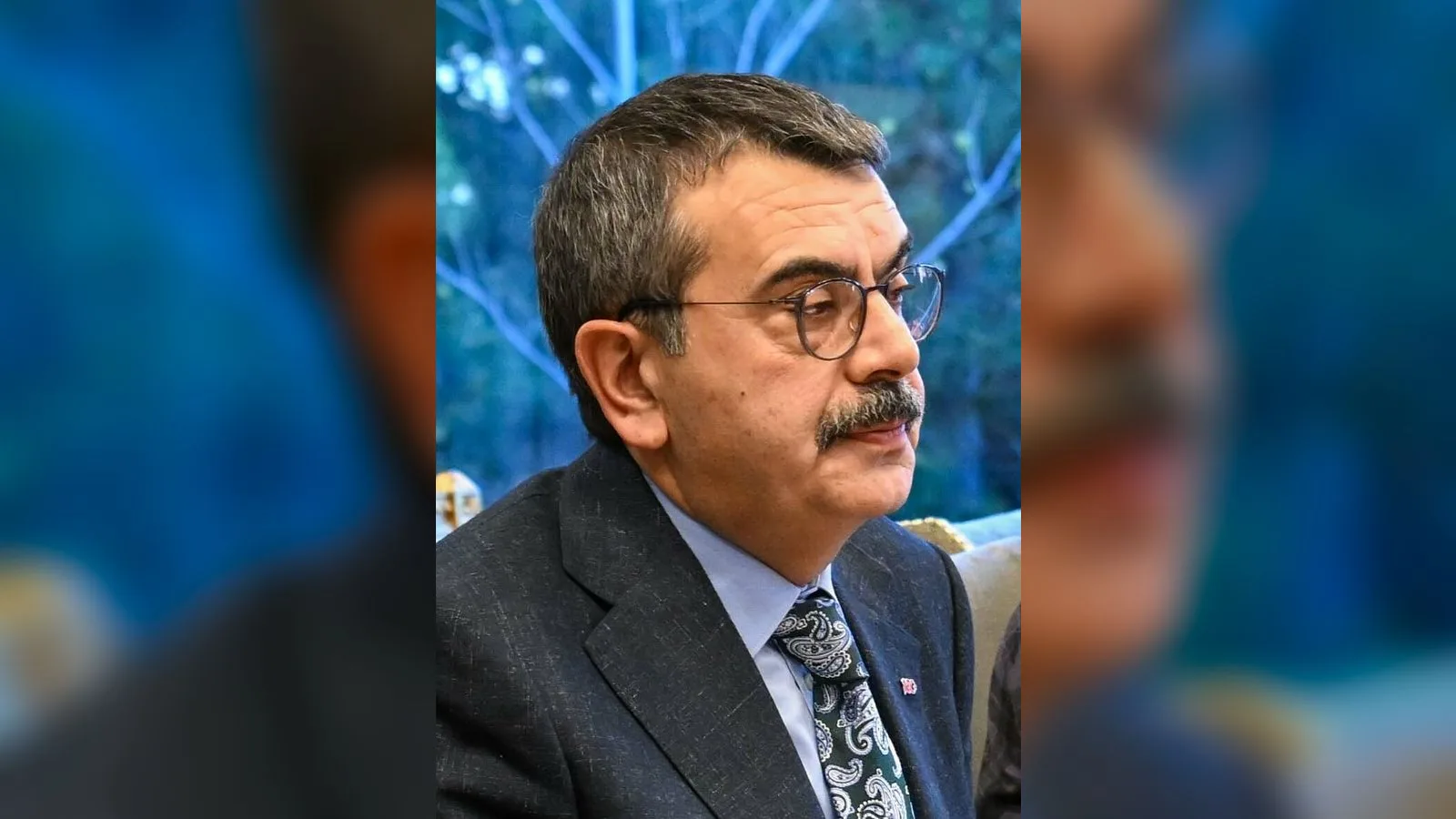 Gözlüklü, takım elbiseli kişinin portresi, mavi arka planında.