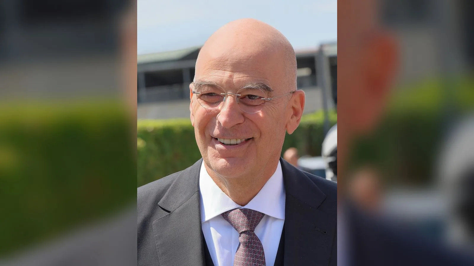Gözlükle takım elbiseli, yaşlı bir erkek, gülümsüyor, dış mekan arka plan.