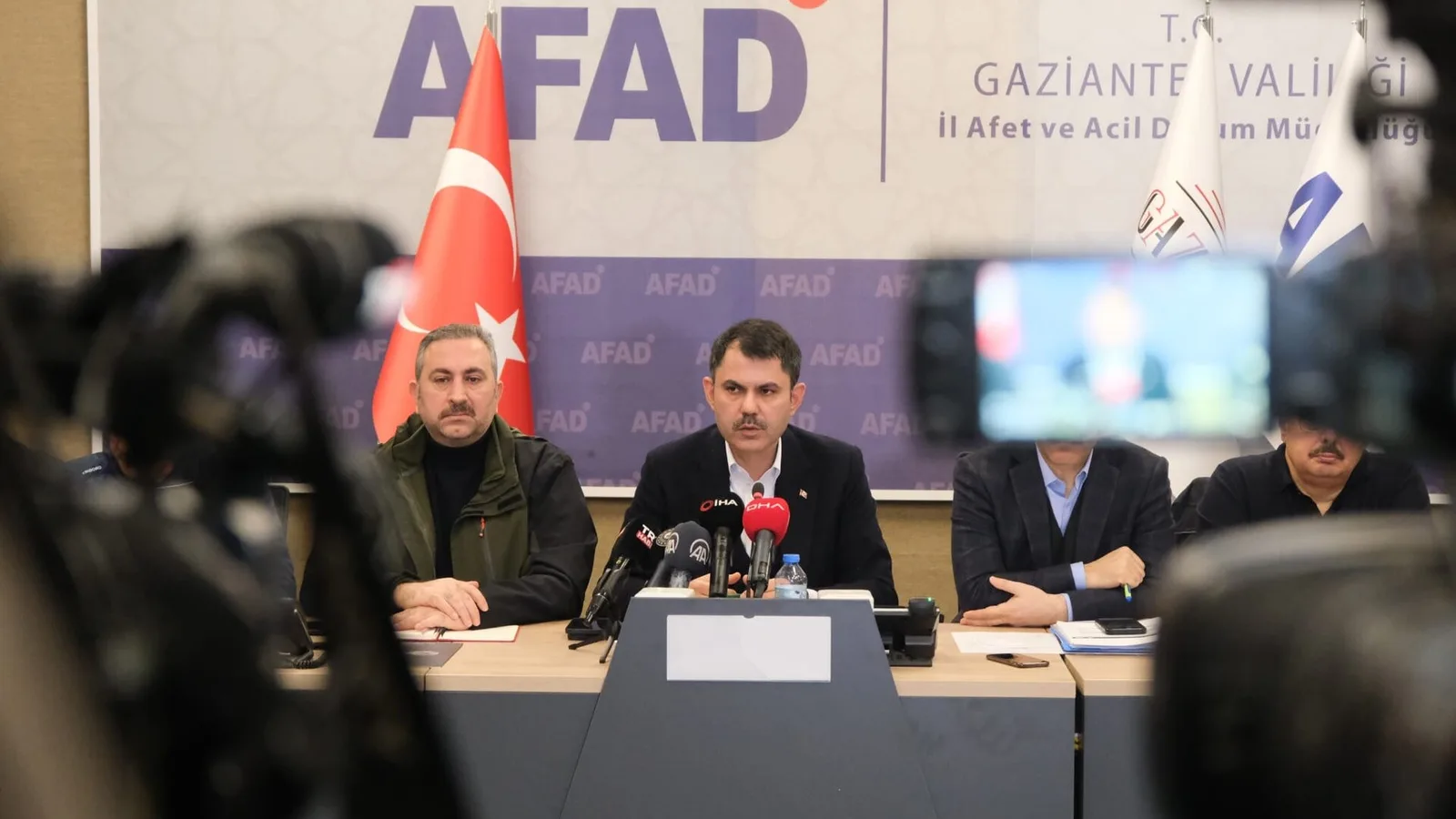 Basın konferansında, AFAD banner arkasında takım elbiseli kişi mikrofonda konuşuyor, kameralar ve dinleyiciler ön planda.