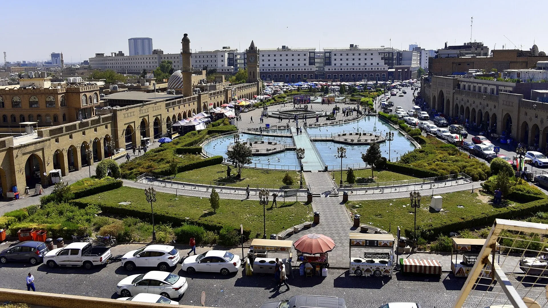 Fırat Nehri'ni çevreleyen, yeşil bahçe ve havuzlu geniş meydan. Sarı taş cami ve hükümet binaları. Şarı arabalar ve insan topluluğu.