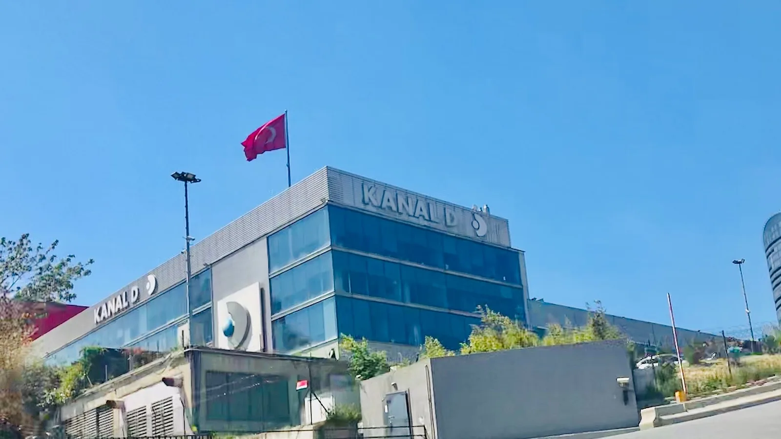 Kanal D logolı çağdaş binasının bahçesi ve girişi, açık hava günü.