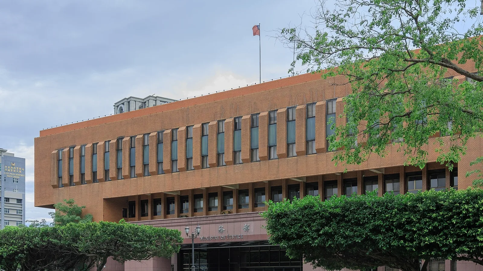 Tuğla renkli, çok katlı resmi bir adli binası avluda ağaçlar arasında.