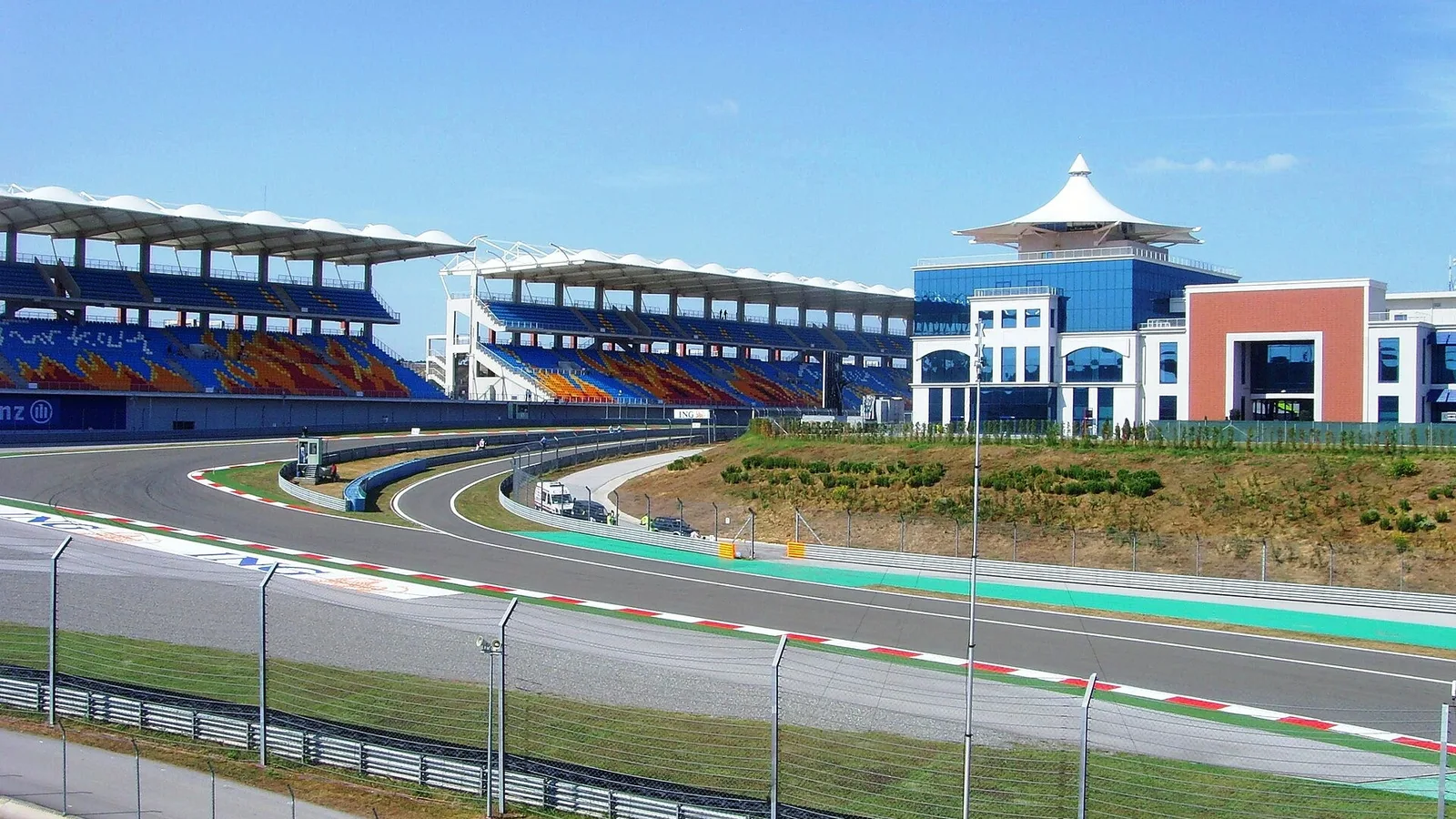 Formula 1 pisti, mavi ve turuncu tribünler, gözlemci platformı ve açık hava.