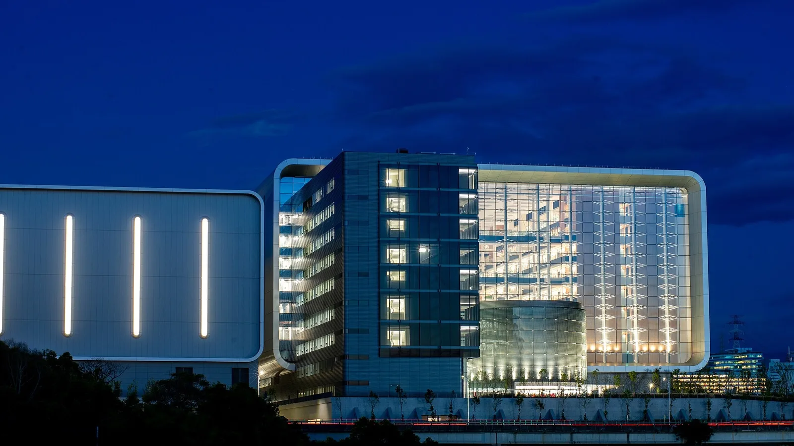 Gece aydınlanan modern ofis binası, suya yansıması görülen mavi işık.