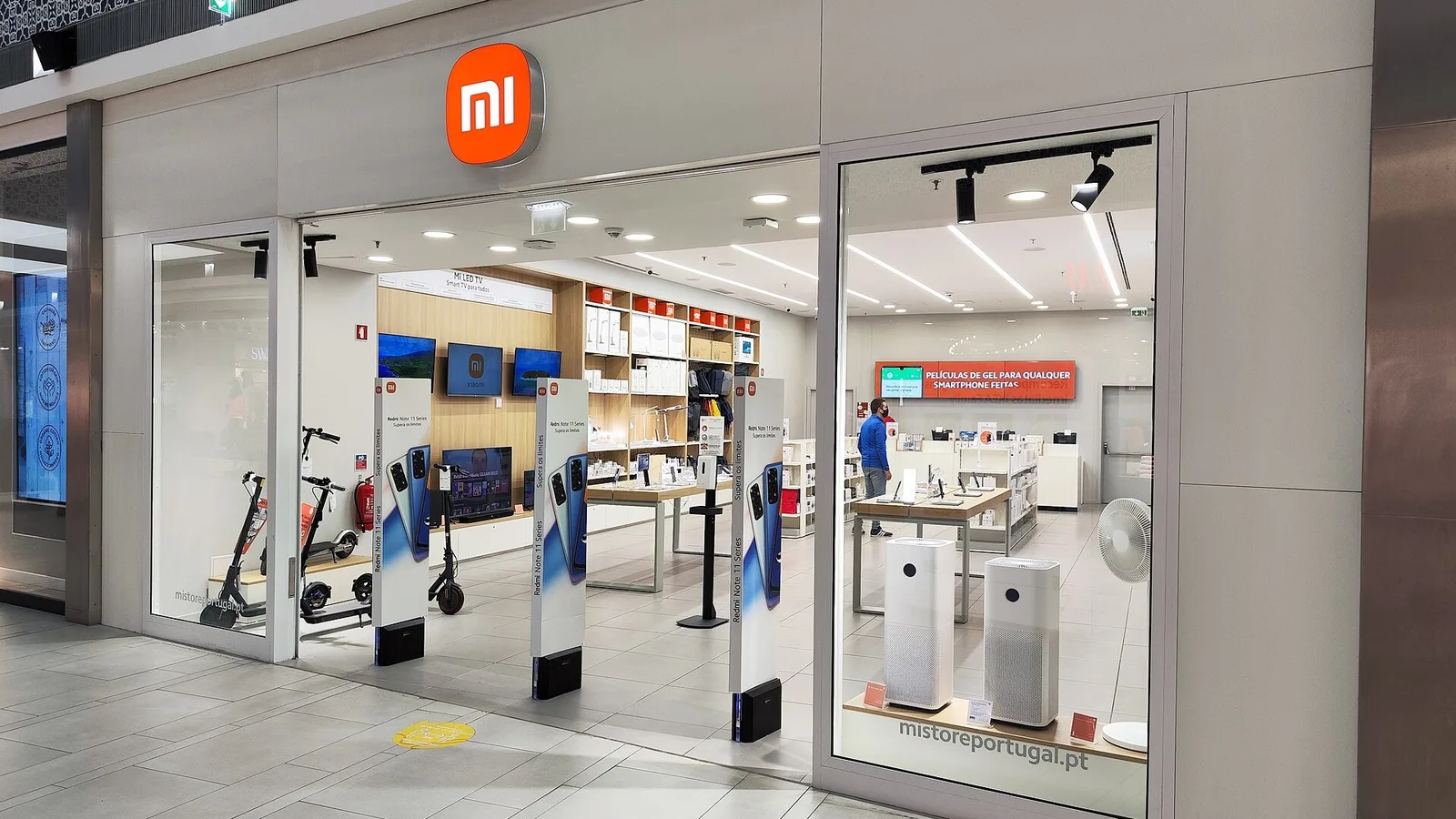 Xiaomi mağazası camlarından iç görünüşü, turuncu logo, ürün serileri ve vitrinler.