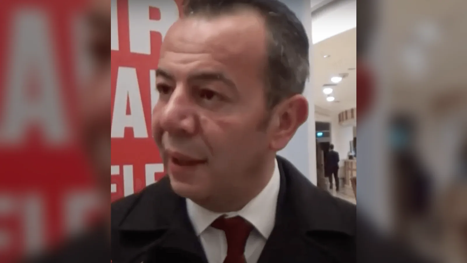 Takım elbiseli, kravatlı erkek portresi, arka planda kırmızı panel.