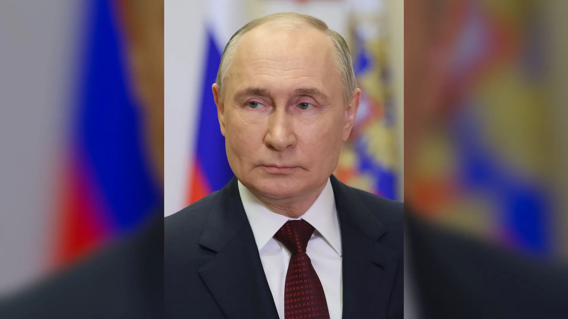 Rus bayrağı önünde koyu takım elbiseli, bordo kravatlı, kel bir adamın portresi
