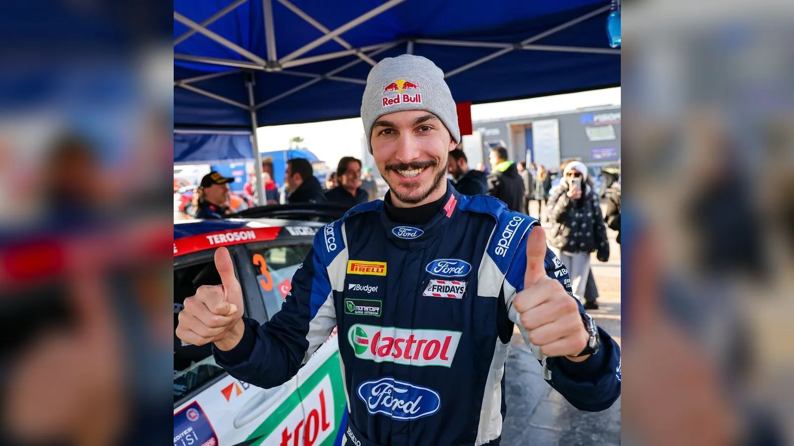 Red Bull şapkası ve Ford yarış elbisesi giymiş, başparmağı kaldırmış şekilde poz veren erkek pilot.