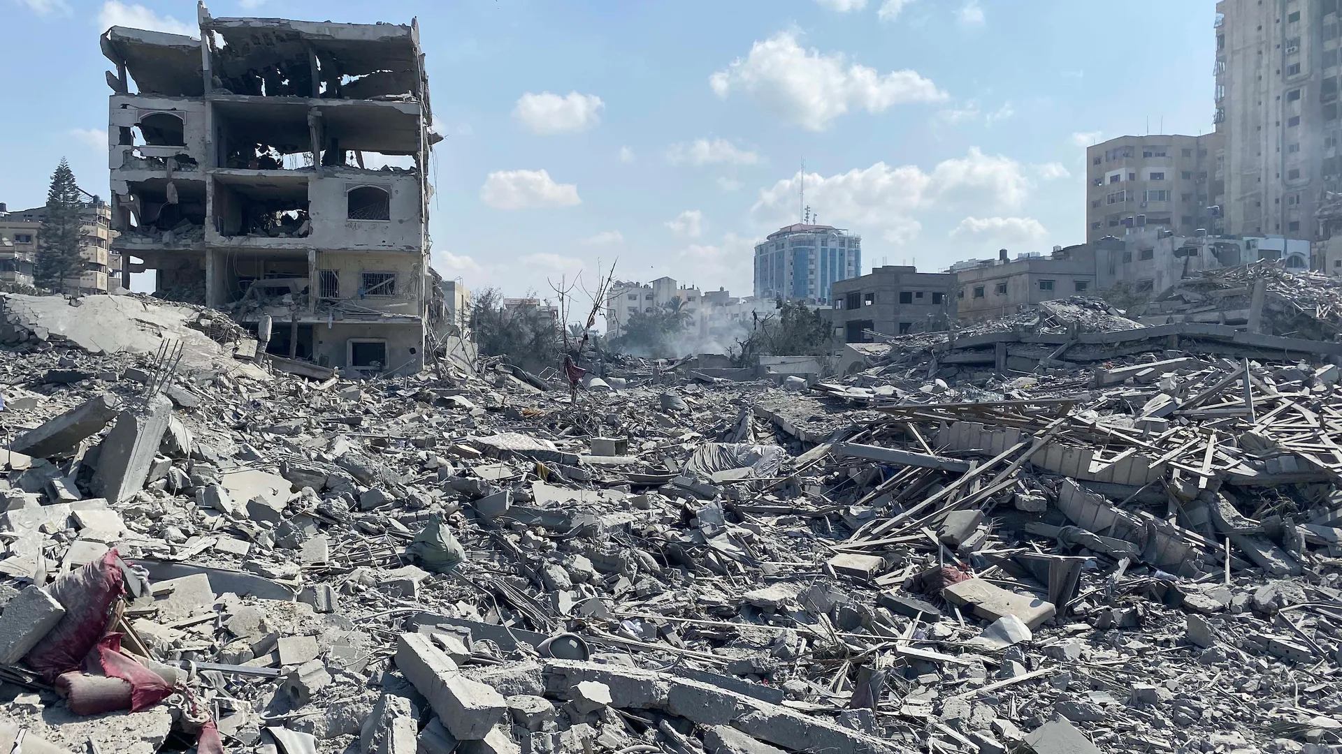 Yıkılmış binaların beton molozları arasında ayakta kalan hasarlı bir yapı ve uzakta yüksek binalar.