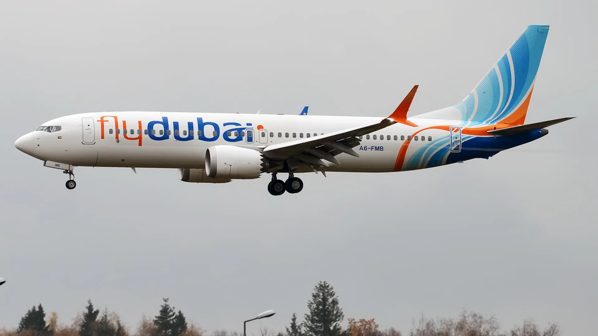 Bulutlu gökyüzünde iniş takımları açık uçan beyaz-mavi-turuncu flydubai yolcu uçağı