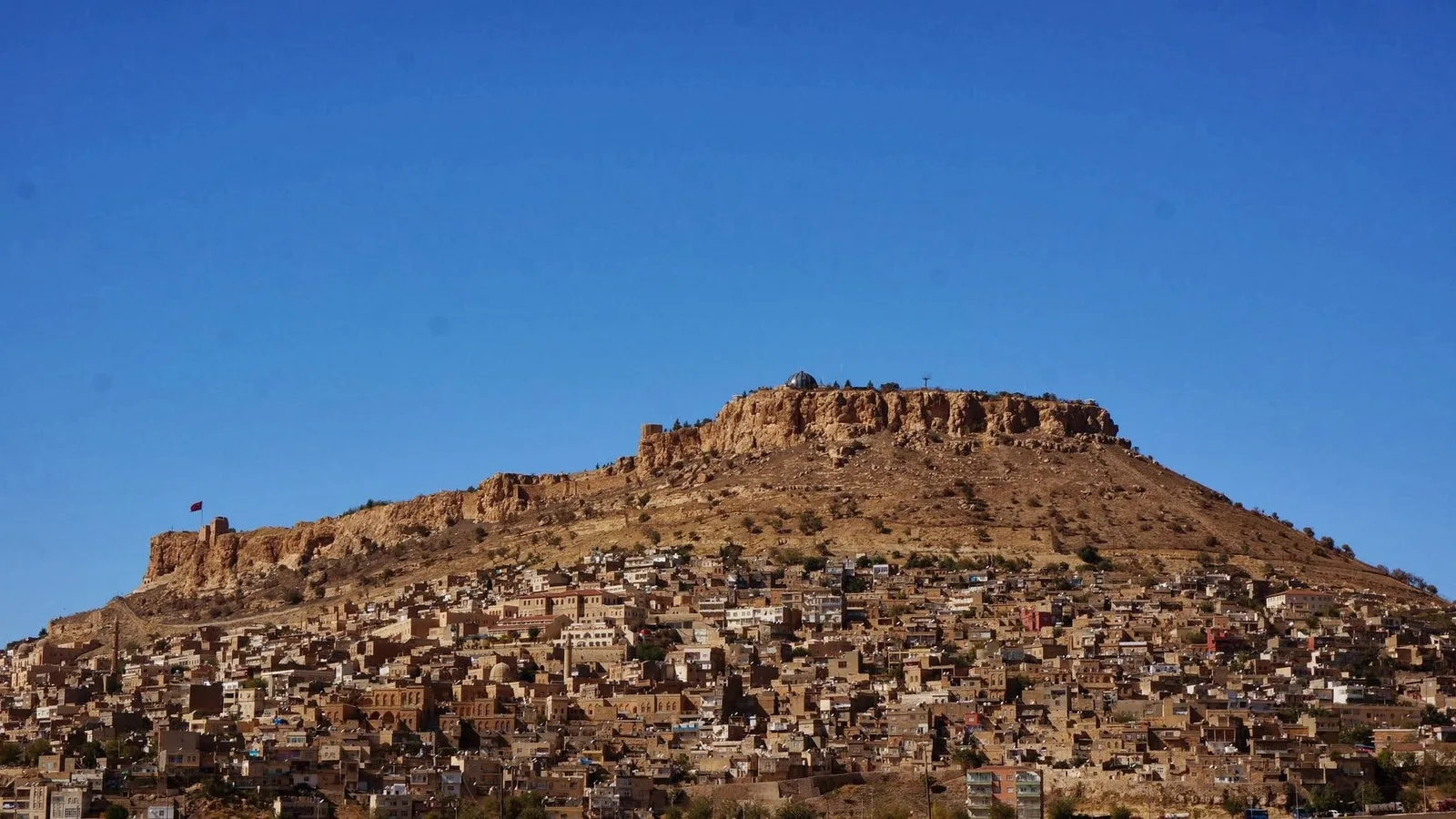 Mardin kentinin tepesi surlarla çevrili, taş evler yamaca yerleşmiş geleneksel şehir manzarası.