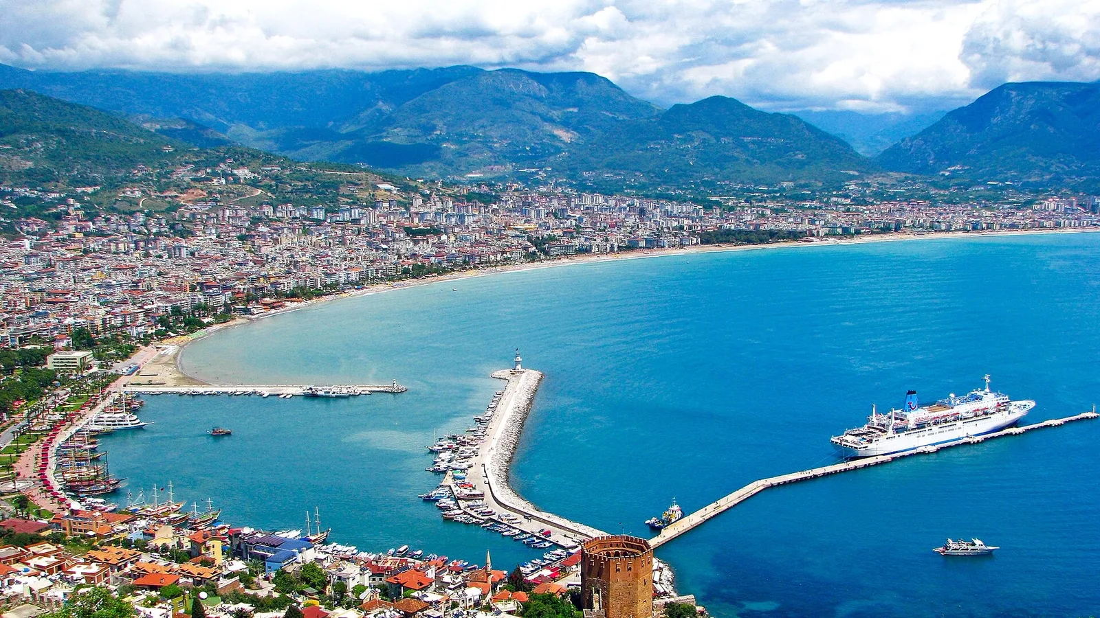 Alanya'nın kuş bakışı görüntüsü, kum plajı, gemi, kırmızı çatılı binalar ve kale.