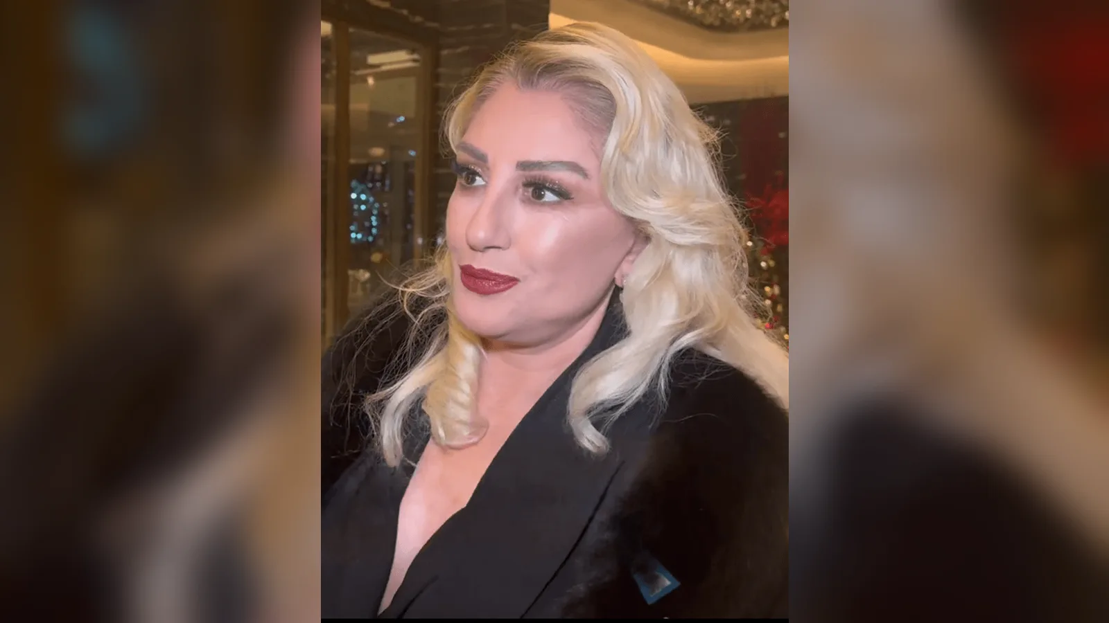 Beyaz uzun saçlı, kırmızı dudaklı bir kadın siyah ceketi ile profil görüş.