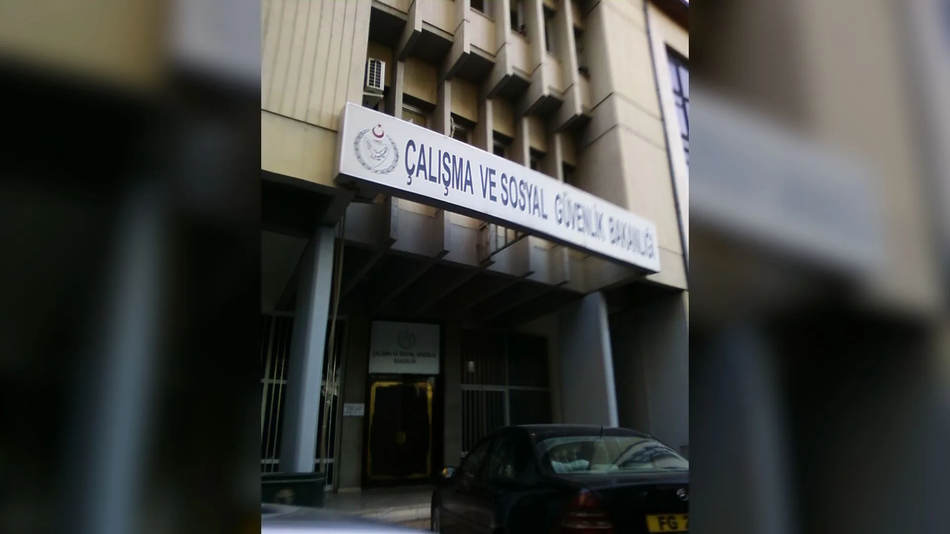 Çalışma ve Sosyal Güvenlik Bakanlığı tabelalı bina girişi, önünde park etmiş siyah bir otomobil