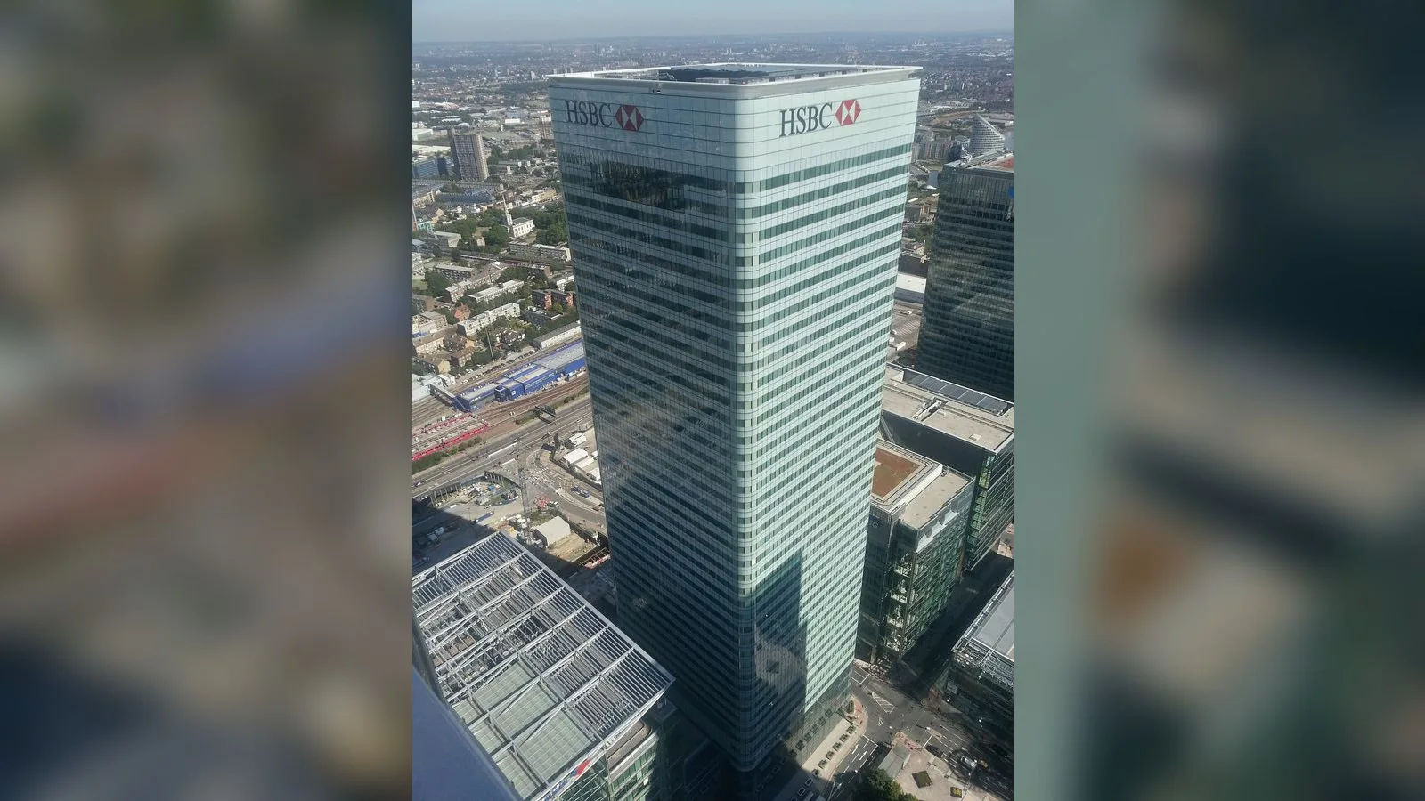 HSBC yazısı olan yüksek ofis binası, şehir arka planında hava fotoğrafı.