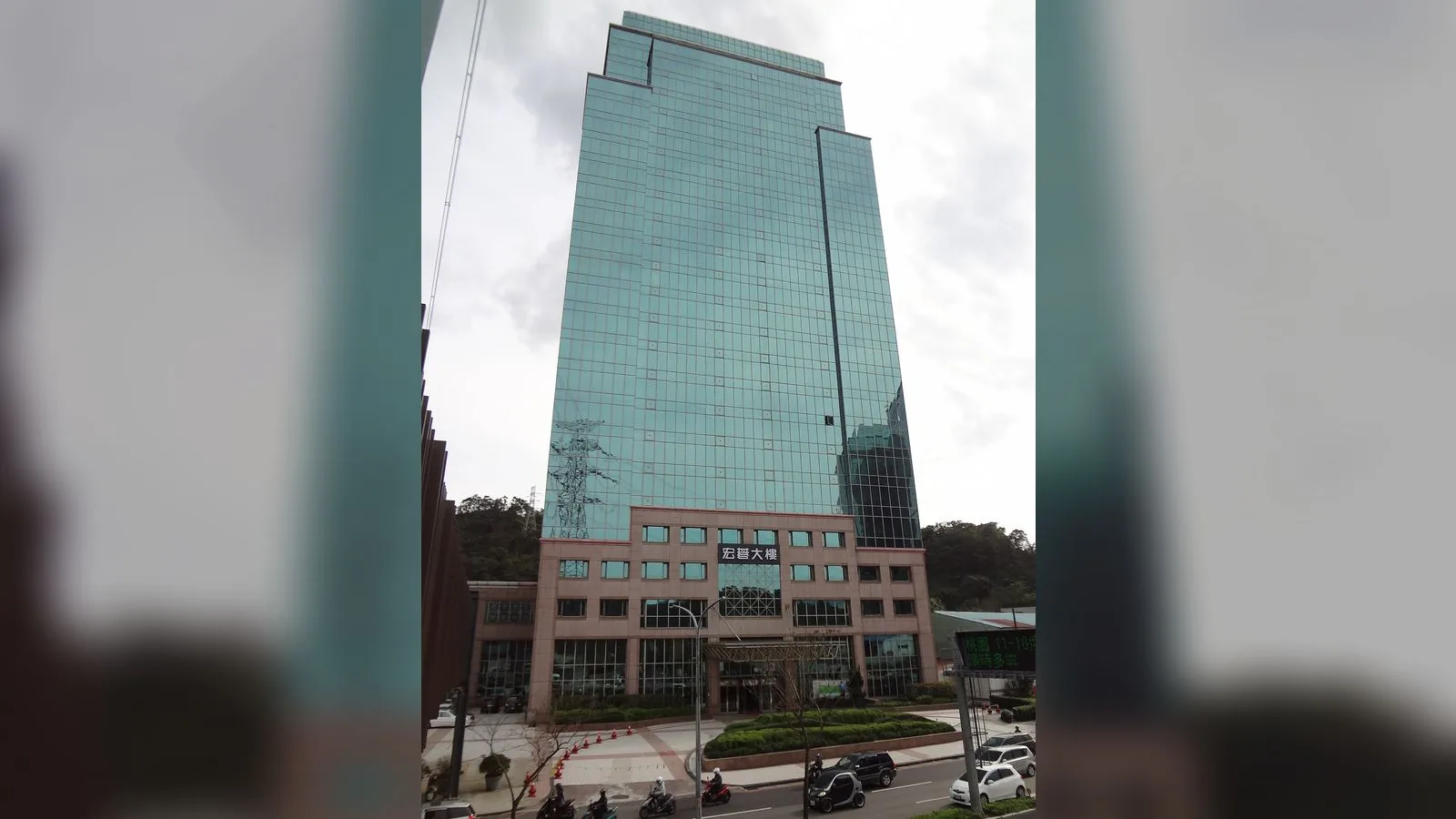 Gözlü camları olan çok katlı bir ofis binası ve alçak katlı turuncu yapı.