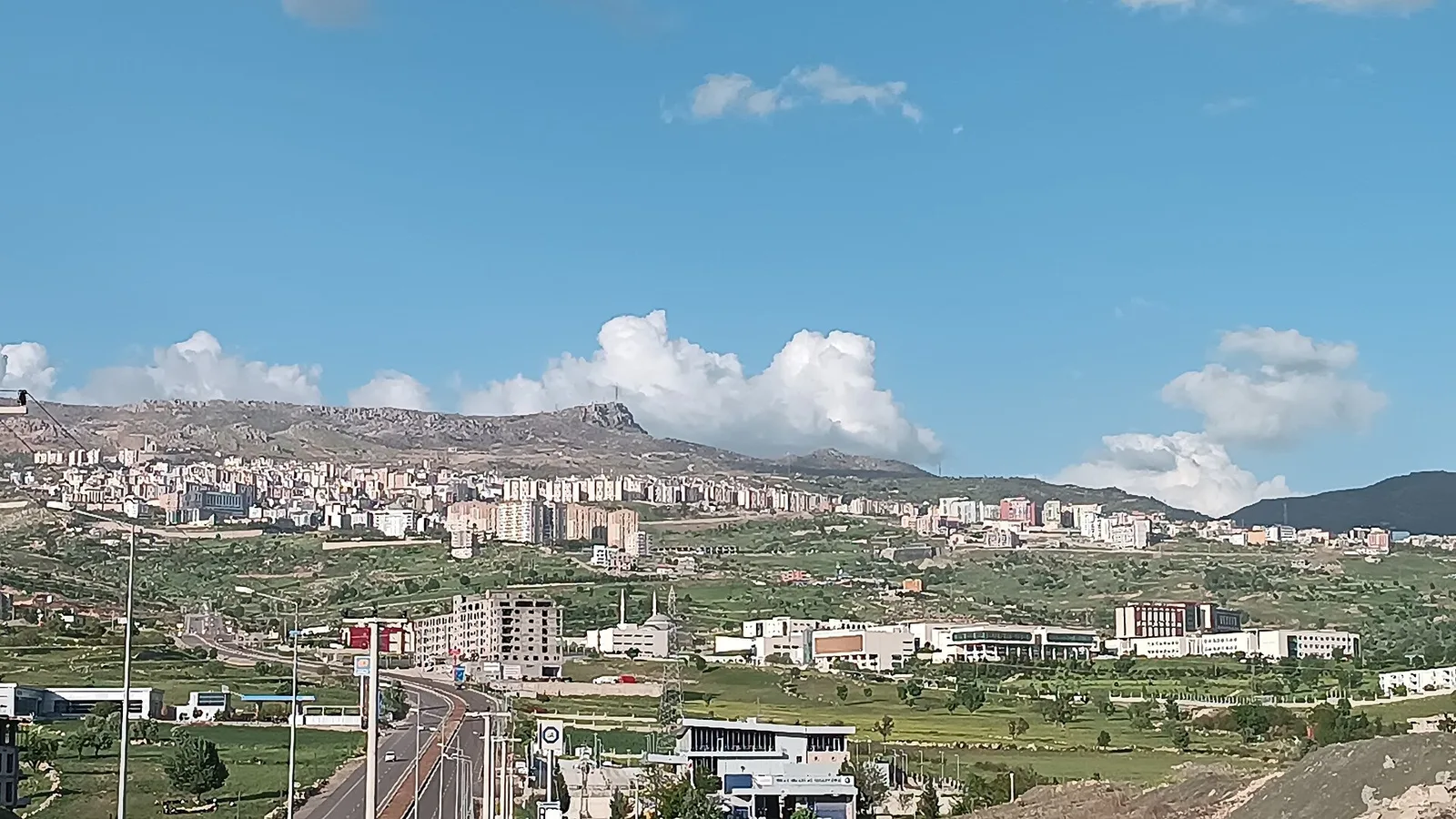 Dağlık bölgede yeşil alanlar ve şehir yapıları manzarası.