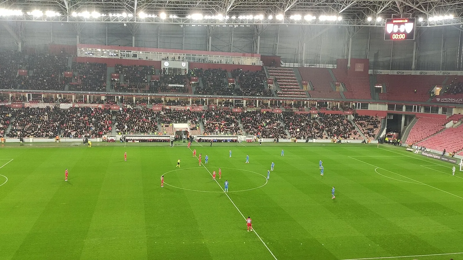 Futbol sahasında maç sırasında oyuncular ve dolmış stadyum tribünleri.