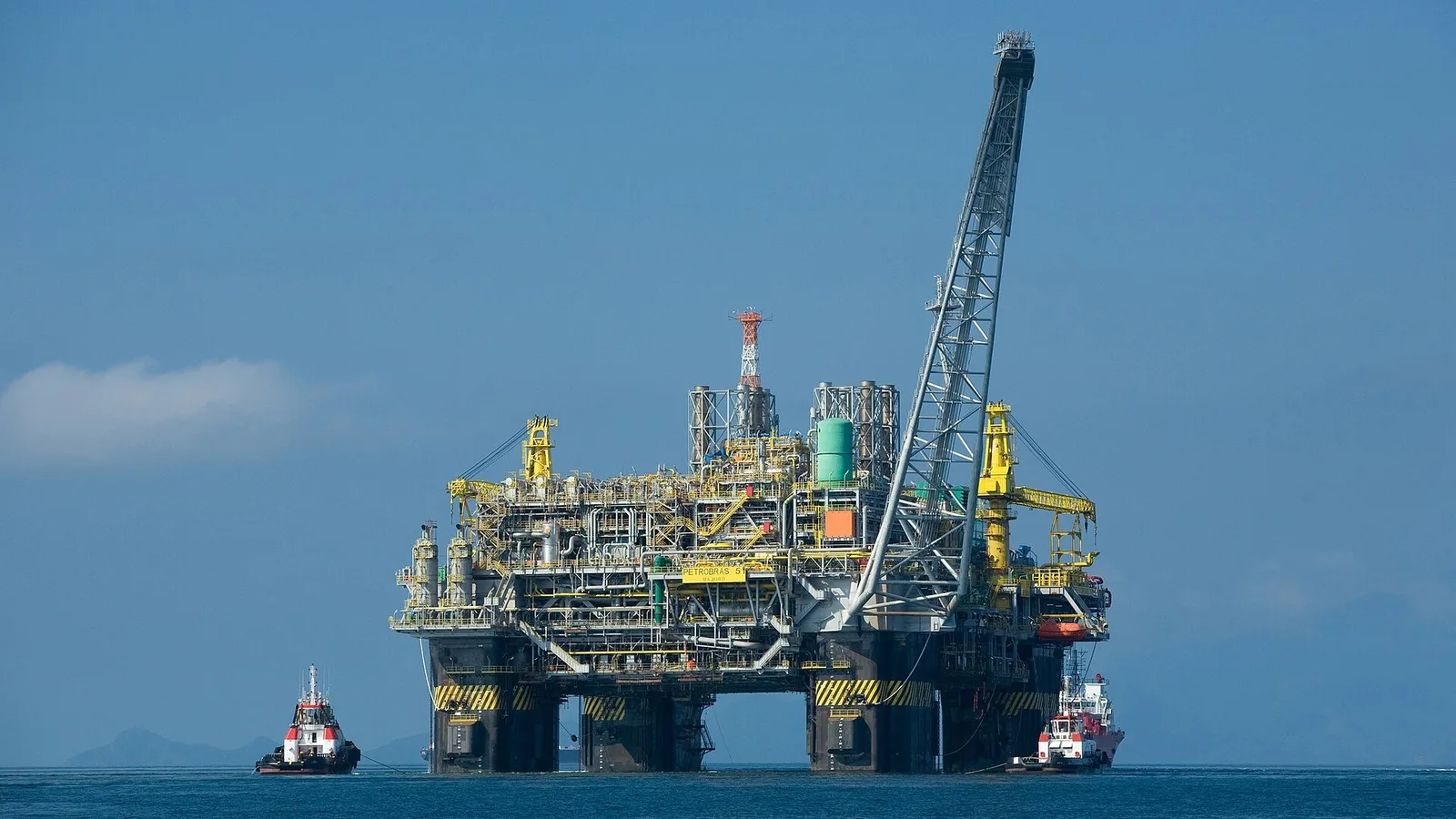 Denizde petrol çıkarma platformu, sarı çerçeveli gemi ve çekici tekneler.