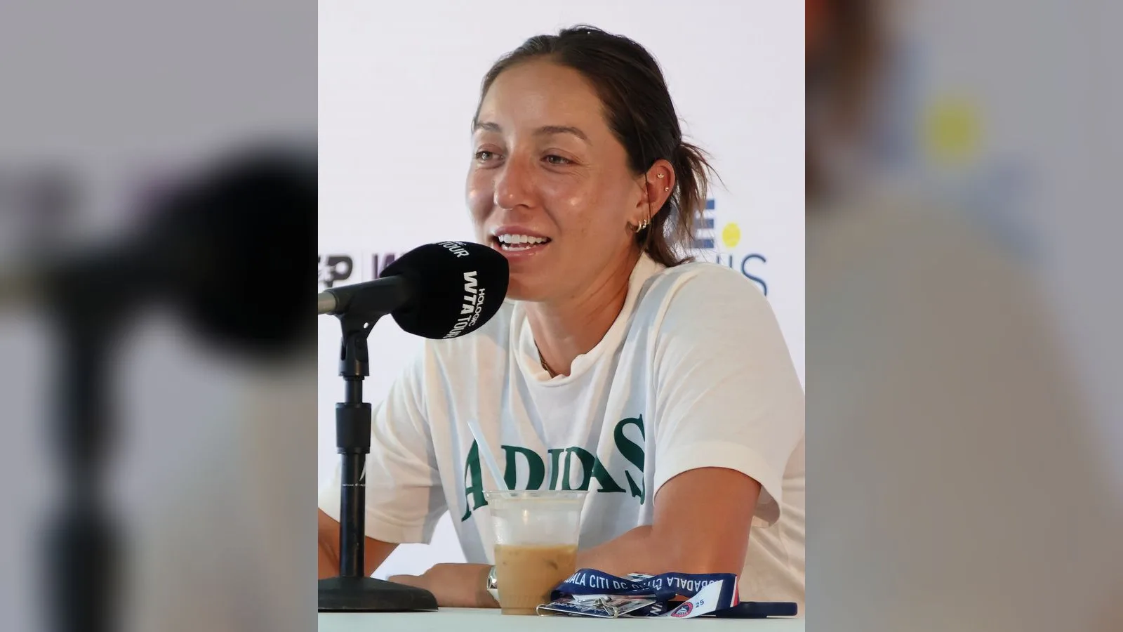 Adidas tişörtü giymiş kadın tenisçi basın konferansında mikrofona konuşuyor.
