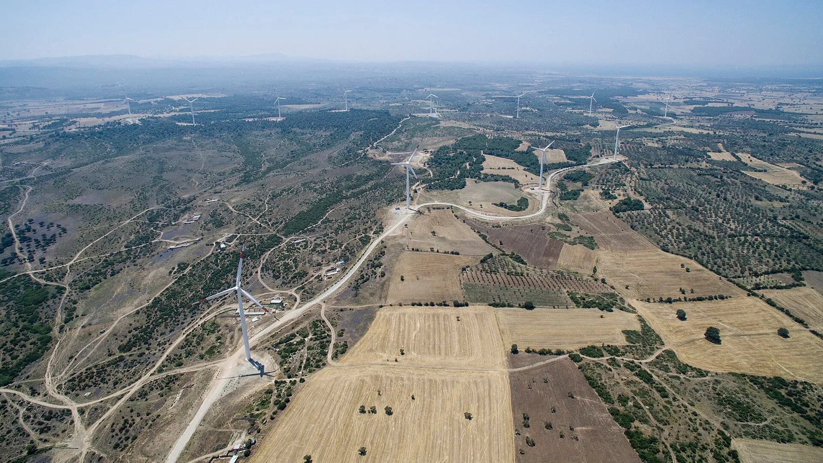 Hava fotoğrafında rüzgar türbinleri ve elektrik direkleri ile tarım arazileri.