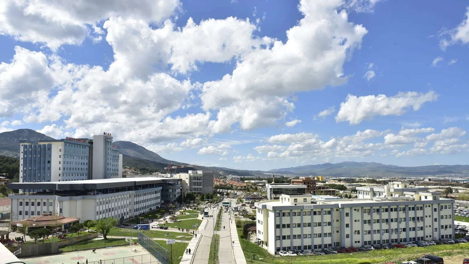 Manisa kampüsü, beyaz binalar, dağ, mavi gökyüzü ve yeşil alan.