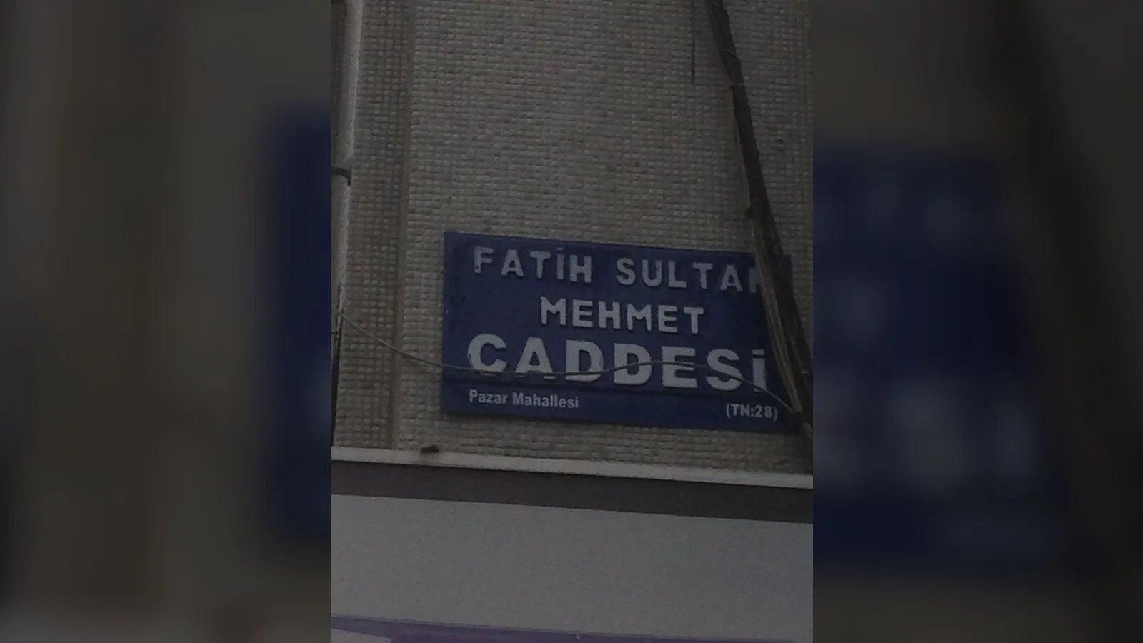 Gri binada Fatih Sultan Mehmet Caddesi sokak ismini gösteren mavi plaka.