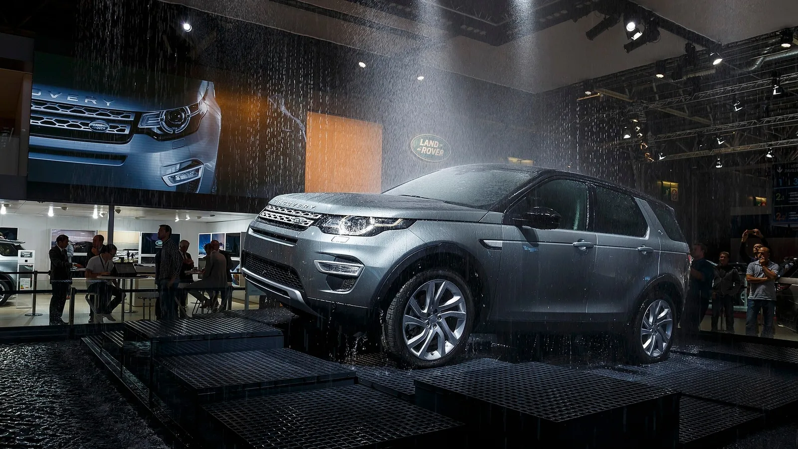 Jaguar Land Rover SUV, fuarın parlak sergisinde, fotoğrafçı ve ziyaretçilerle çevrili.