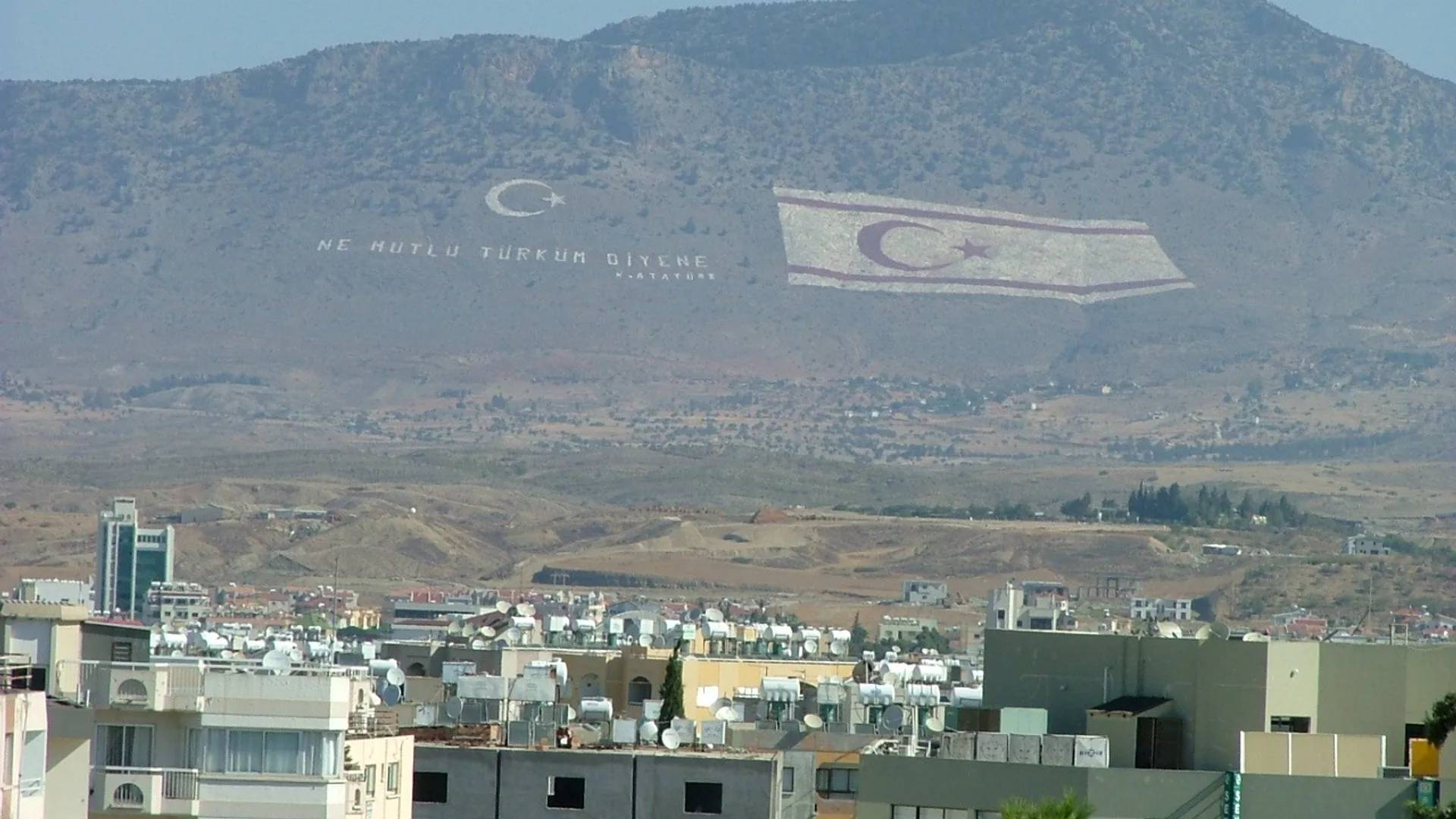 Girne şehrinin üzerindeki gökyüzünde Türk bayrağı ve ay-yıldız şekilli flamalar asılı duruyor.