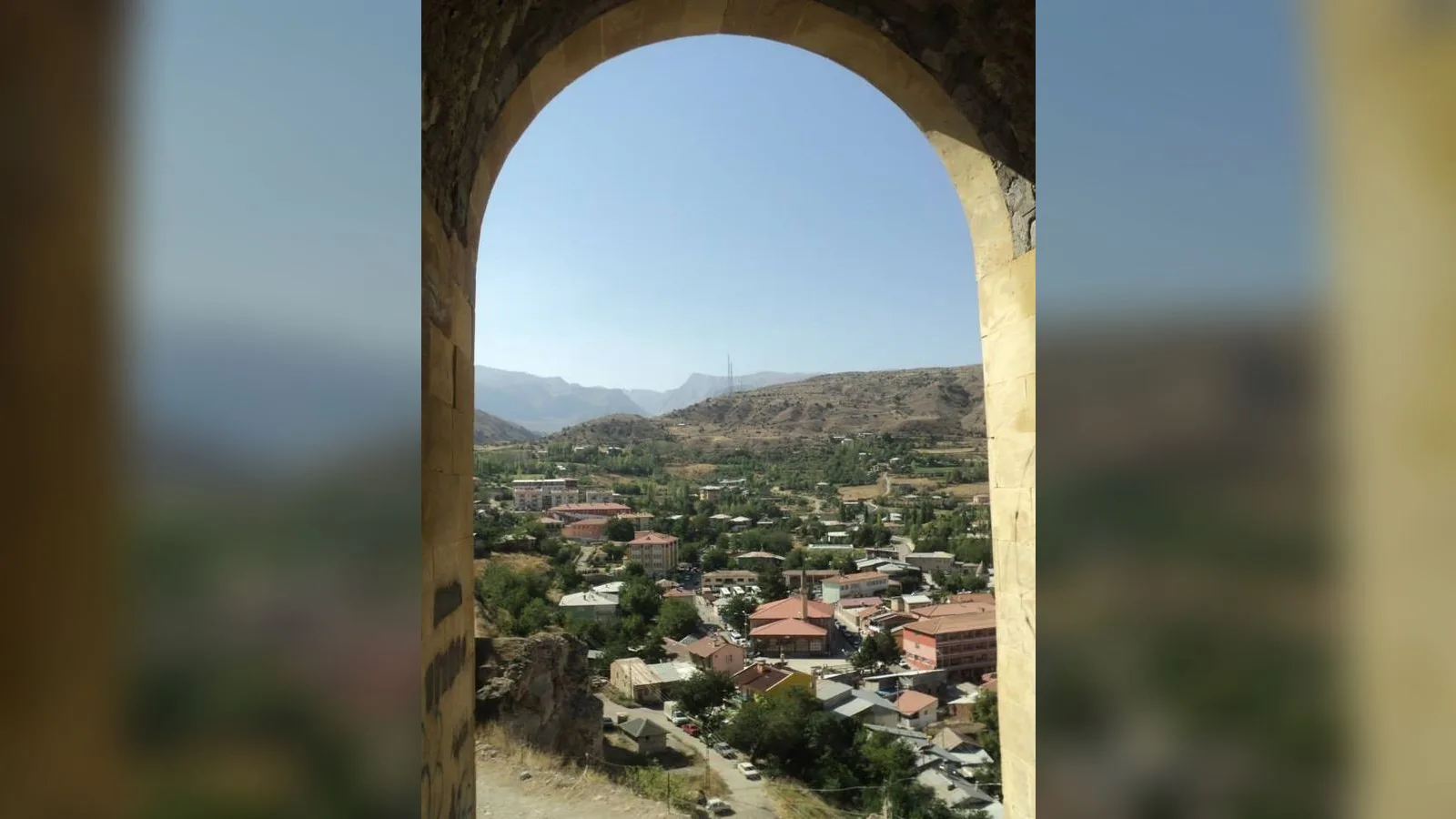 Taş kemer arkasından gözüken dağlı kasaba manzarası.