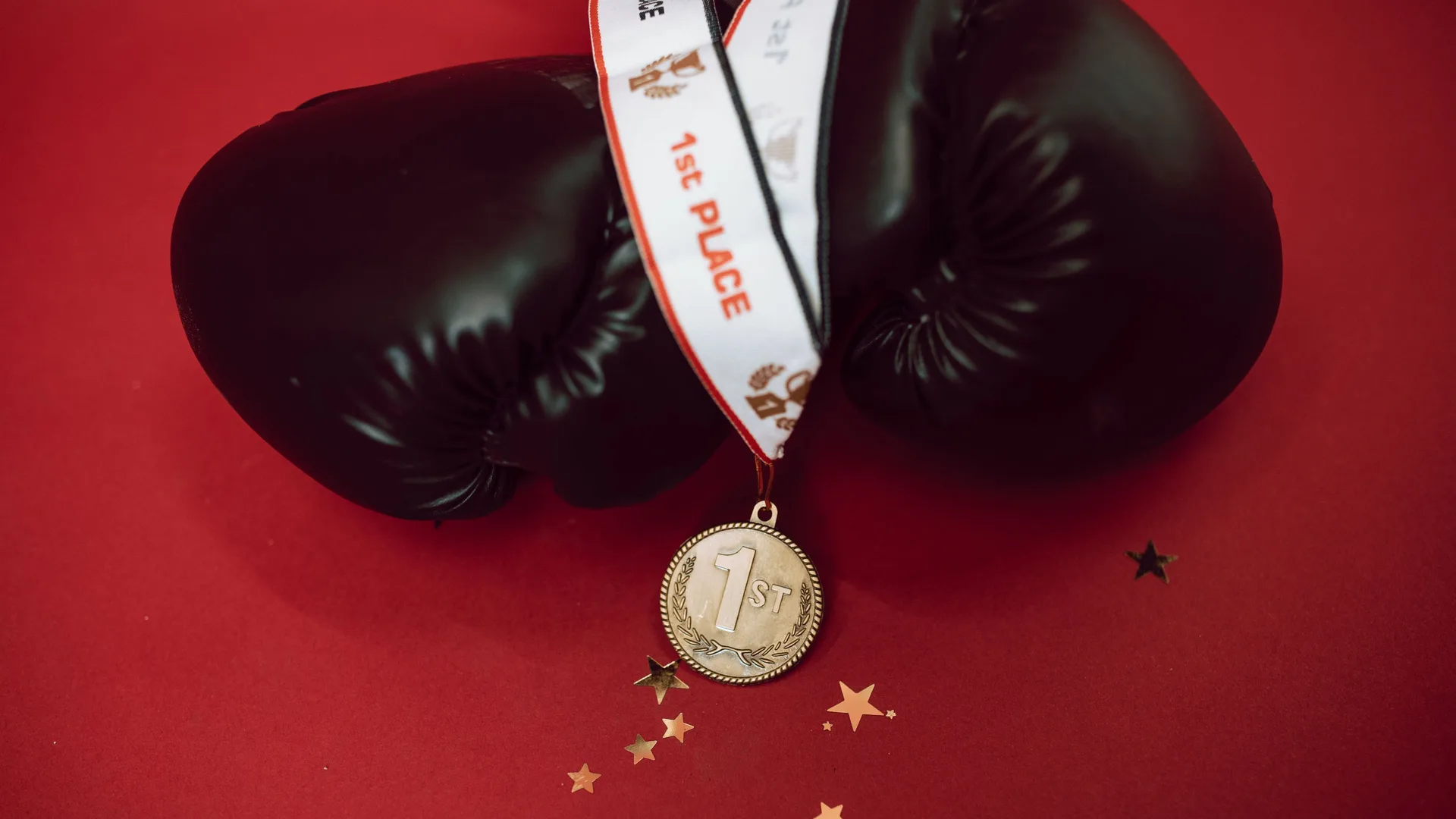 Kırmızı zemin üzerinde siyah boks eldivenleri ve "1st" yazan birincilik madalyası