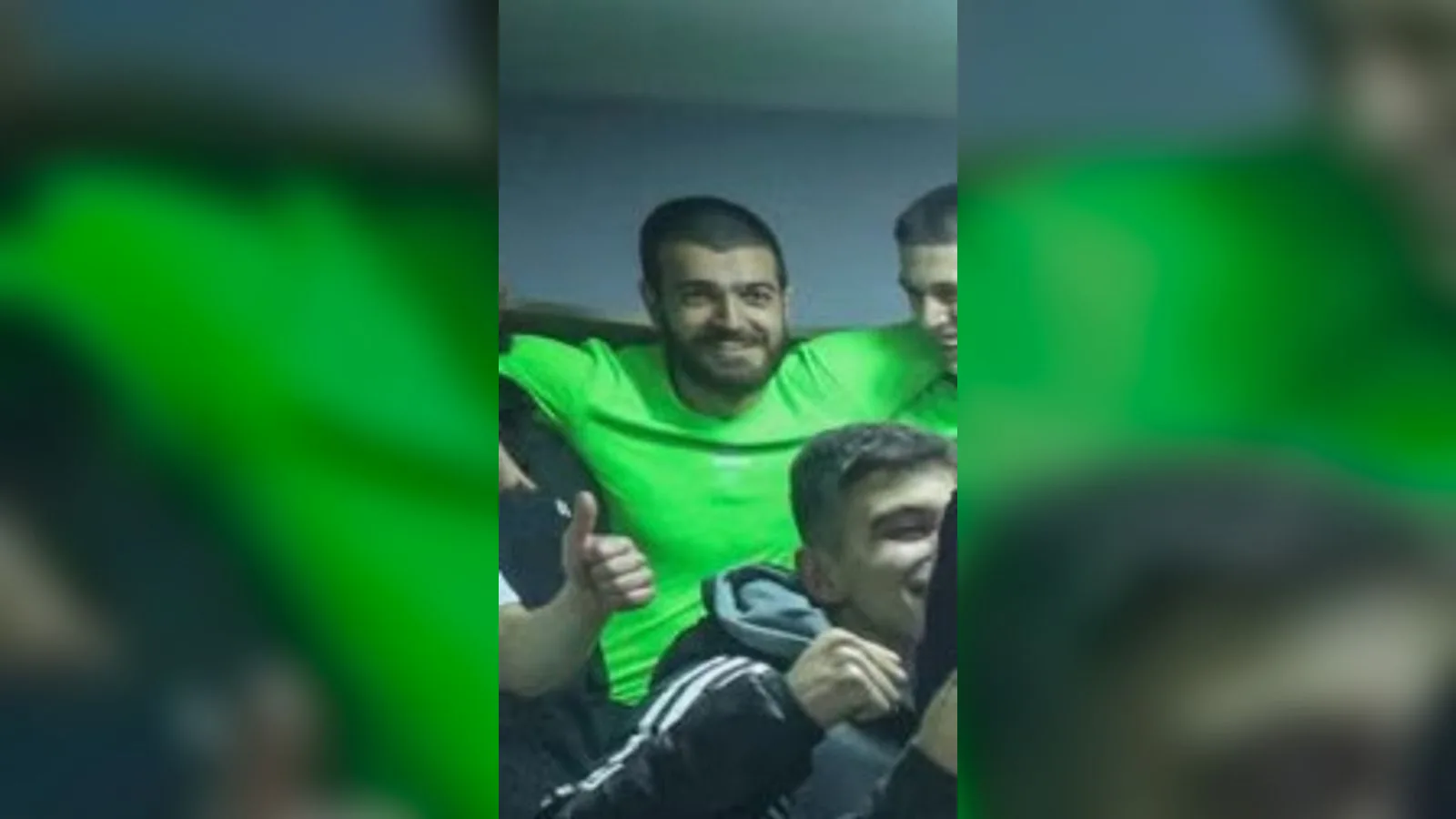 Yeşil formalı futbolcu taraftarlar arasında elini kaldırarak pozlar.