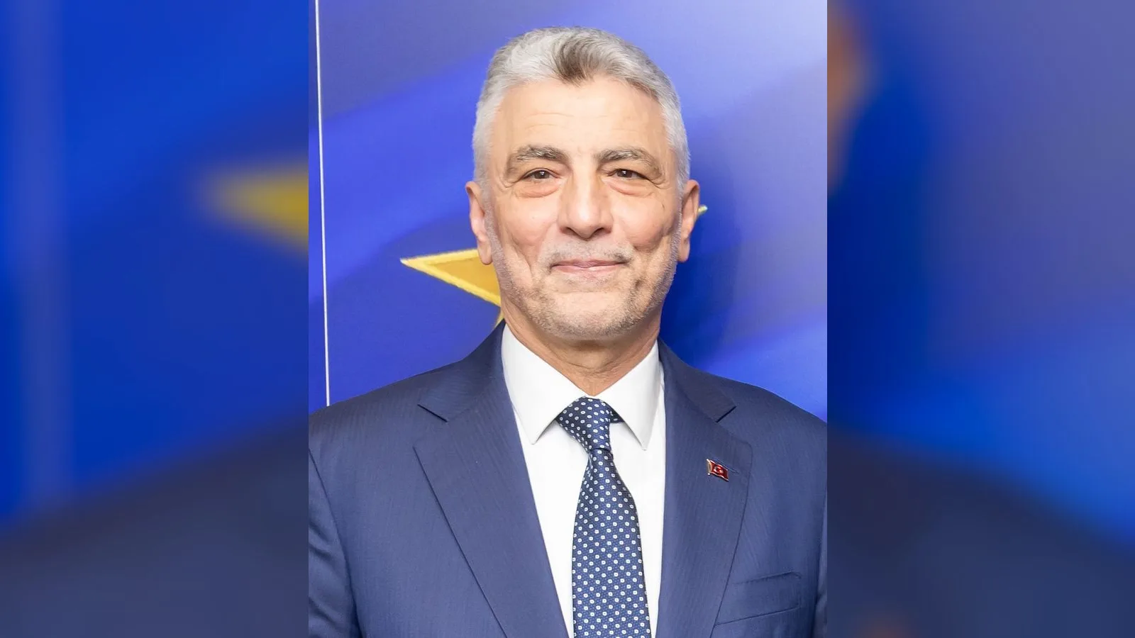 Takım elbiseli, kravatlı ve rozet takılı orta yaşlı bir erkek.