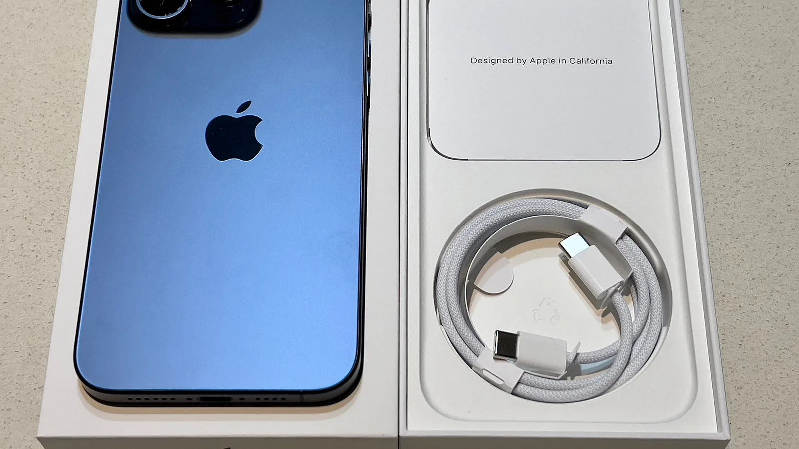 Açık mavi ekranlı ve kablolu şarj cihazı içeren açılmış iPhone kutusu.