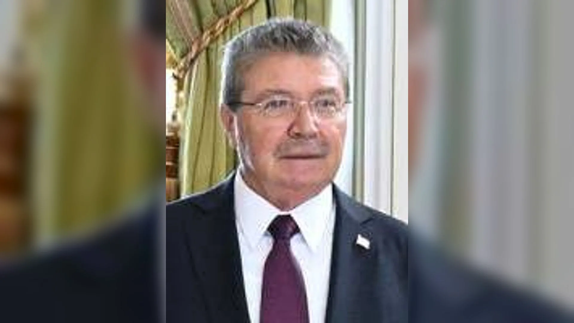 Gözlüklü, gri saçlı, takım elbiseli ve bordo kravatlı bıyıklı bir adam