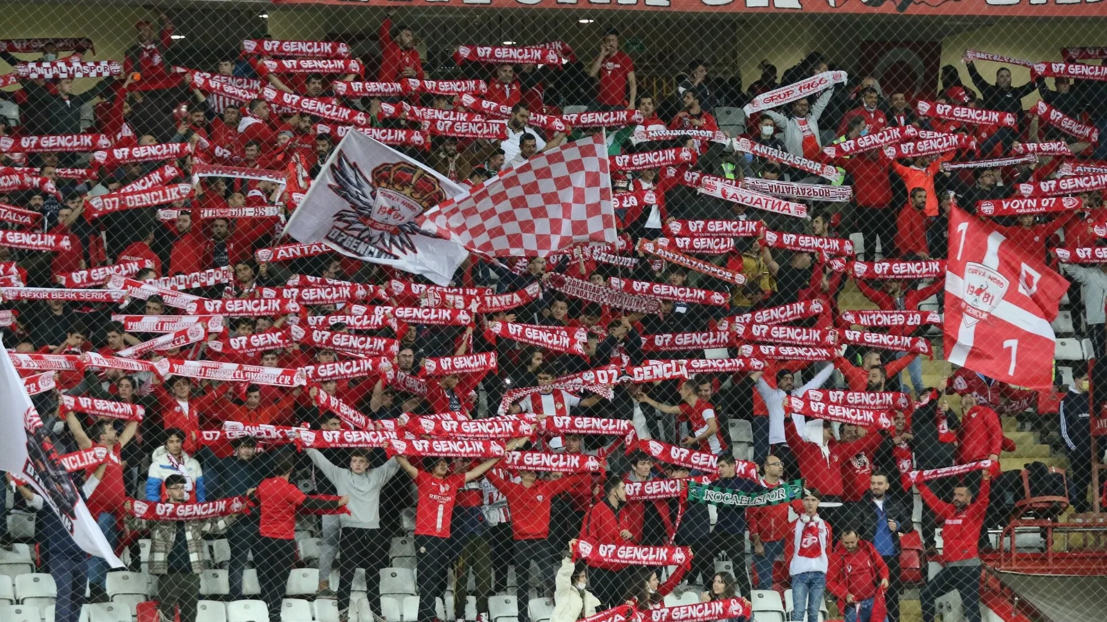 Futbol stadyumunda Antalyaspor taraftarları tribünde sancak ve bez tutuyor.