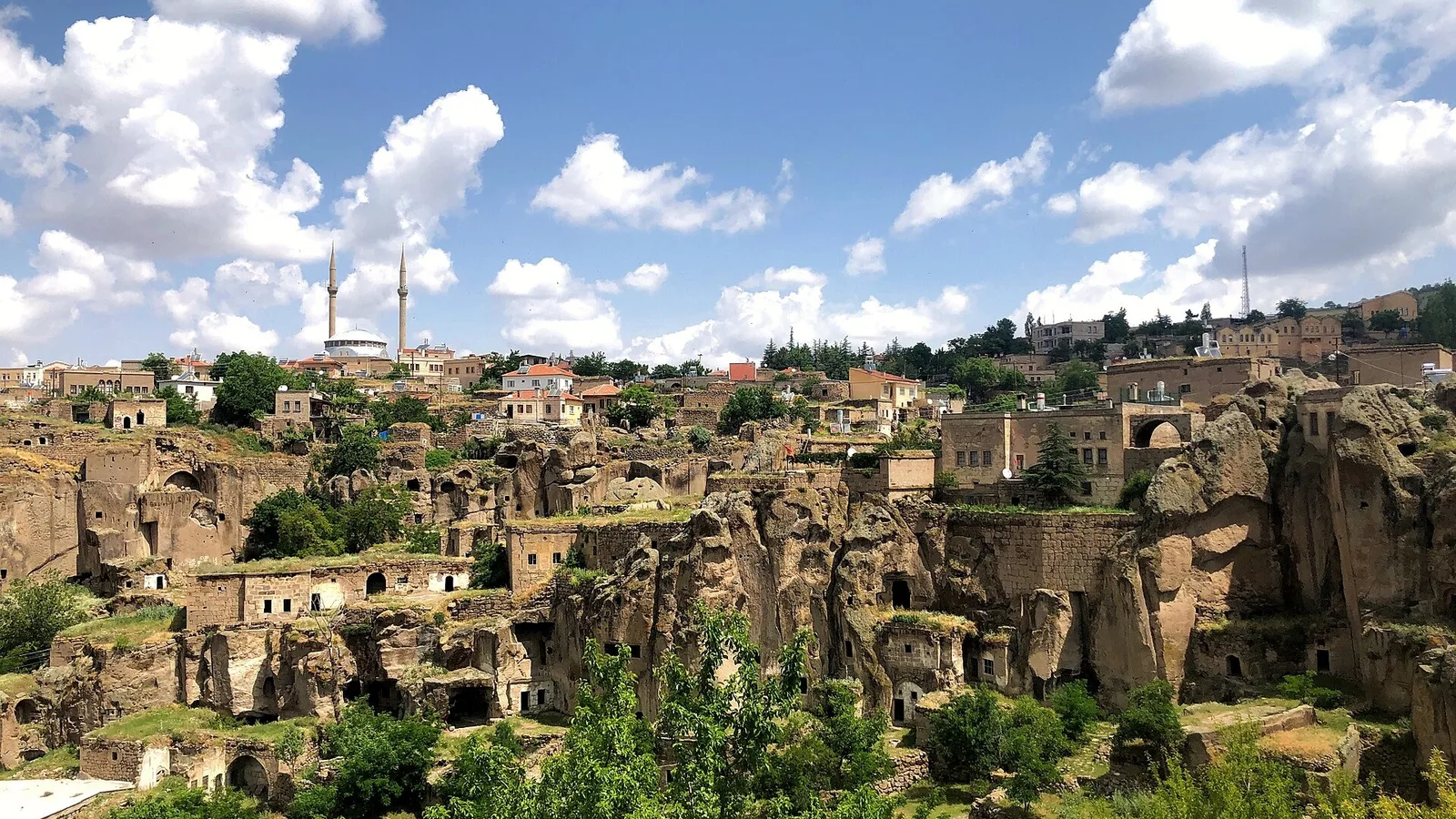 Güzelyurt şehrinin genel görünümü, ön planda kaya formasyonları, arka planda minareliyle şehir manzarası.