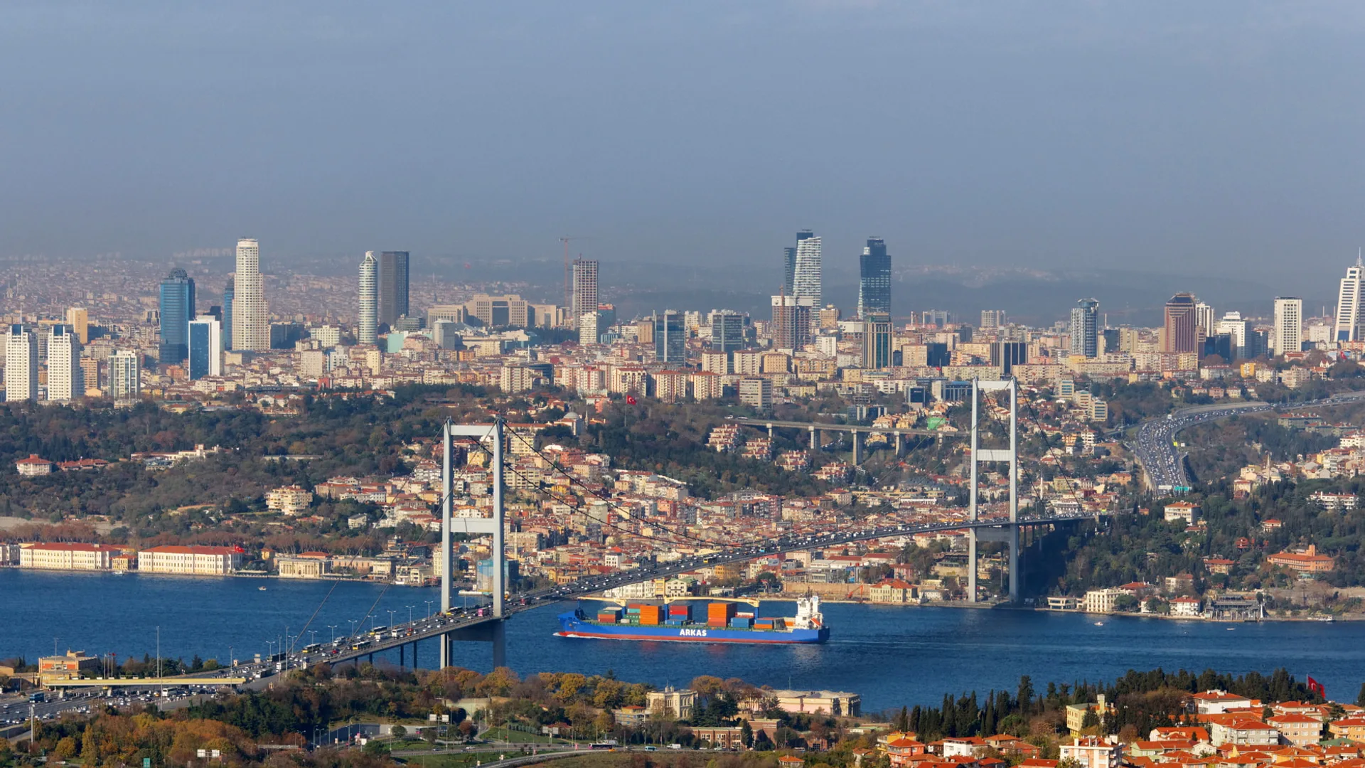 Boğaz Köprüsü, altından geçen konteyner gemisi ve arkada gökdelenlerle dolu şehir silueti