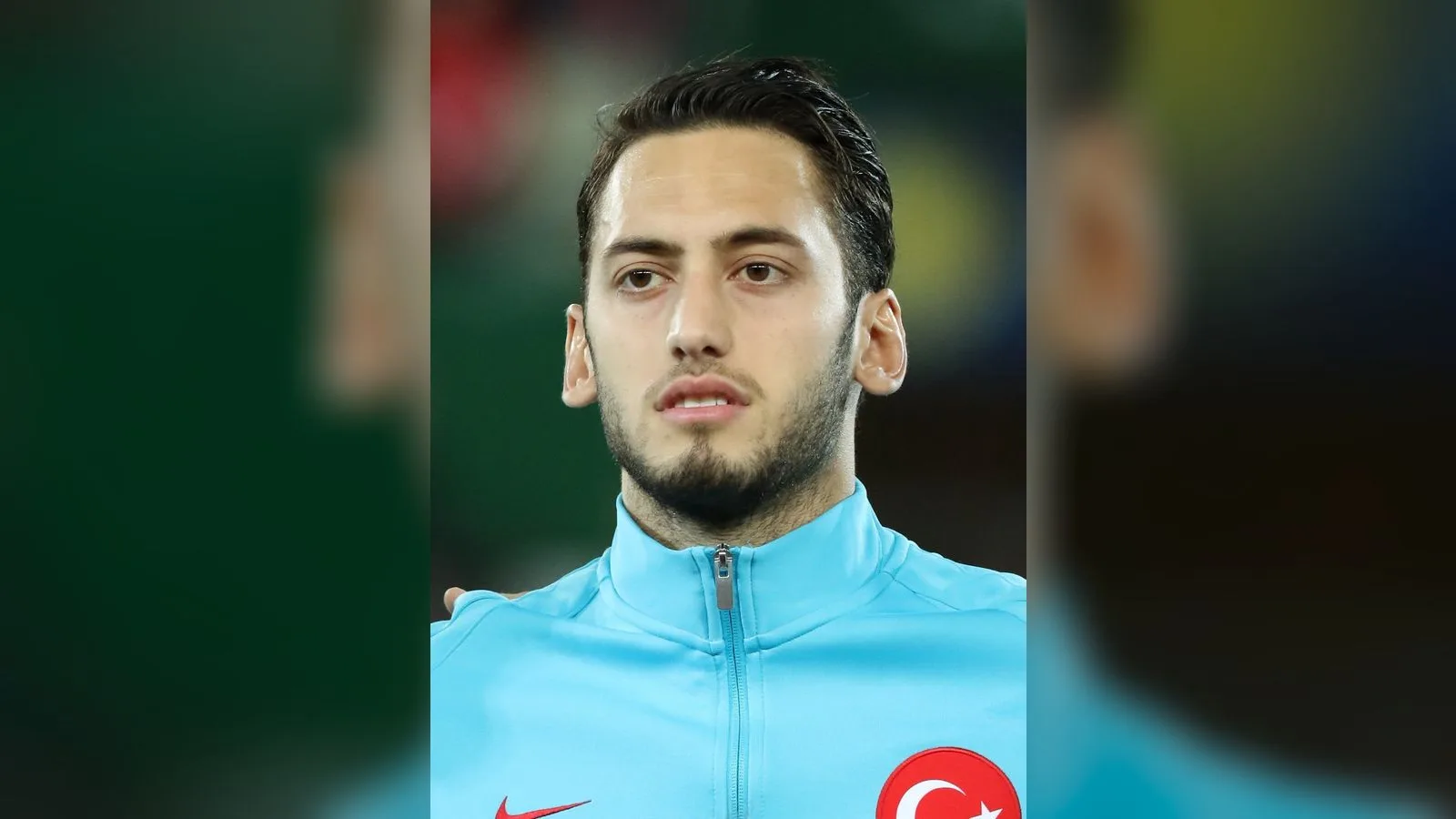 Mavi antrenman formasıyla futbolcu portresi, göğsünde Türkiye bayrağı rozeti.
