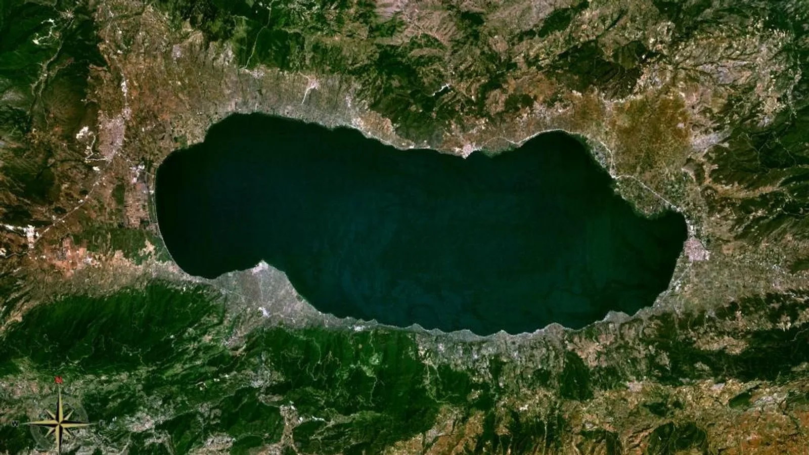 Göl ve çevresinin uydu görüntüsü, yeşil ormanlarla kuşatılmış koyu su.
