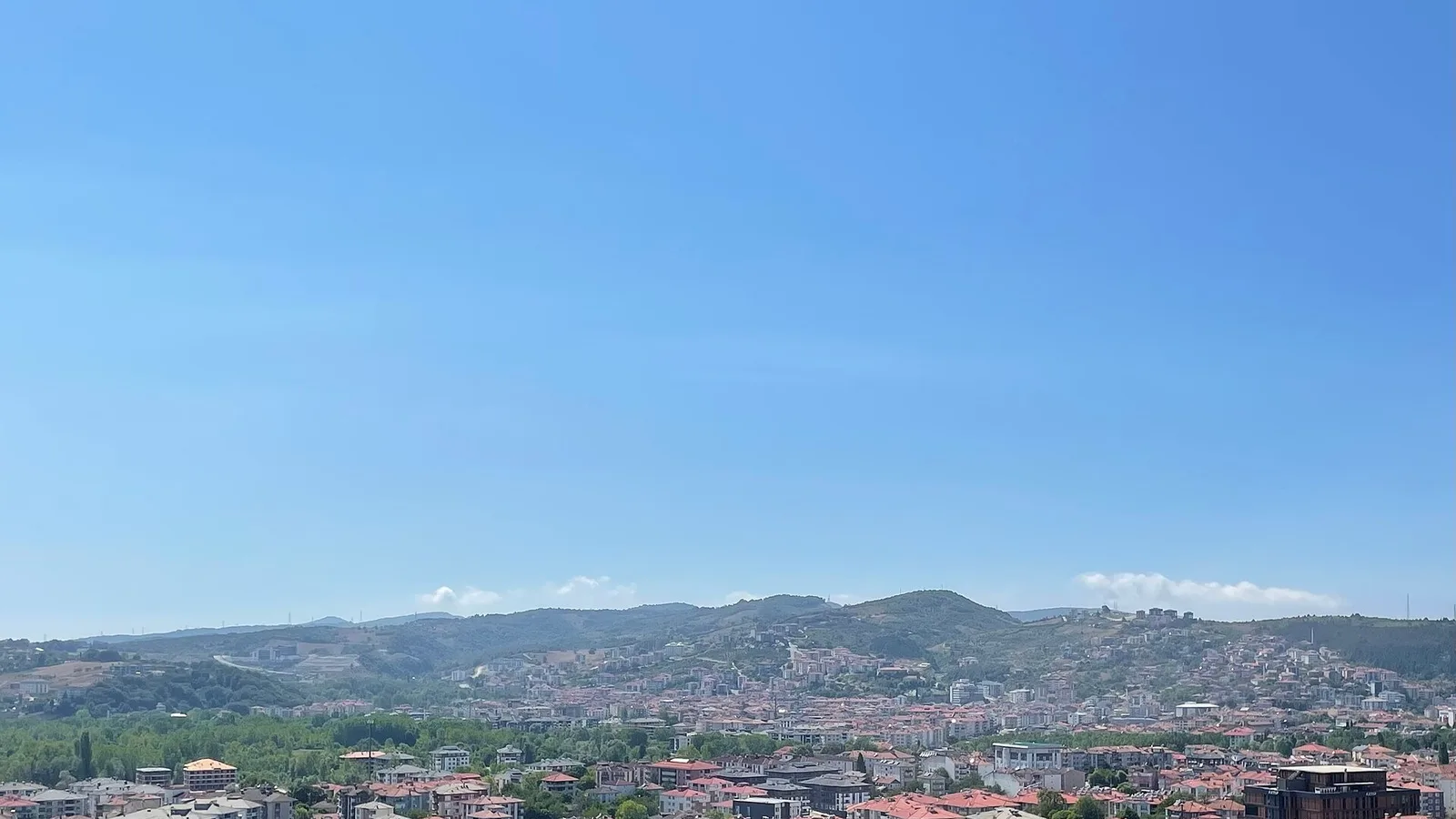 Dağlık bölgede kırmızı kiremitli evlerin yoğun olduğu şehir manzarası, açık mavi gökyüzü altında.