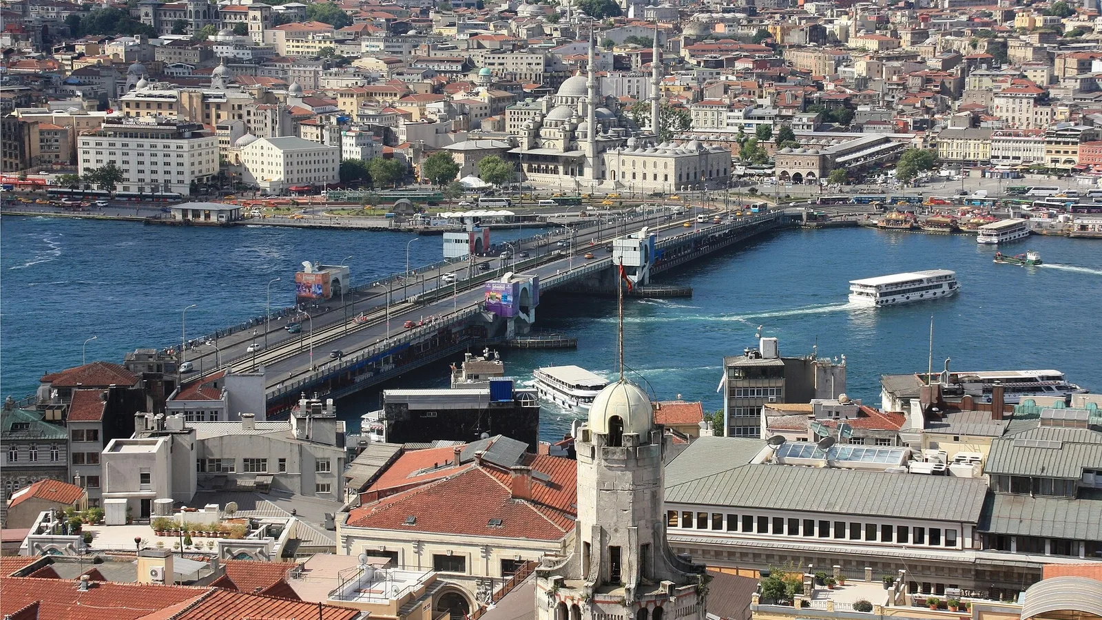 Boğaz köprüsü, liman ve gemi iskeleleriyle İstanbul manzarası, ön planda kubeli bir bina.
