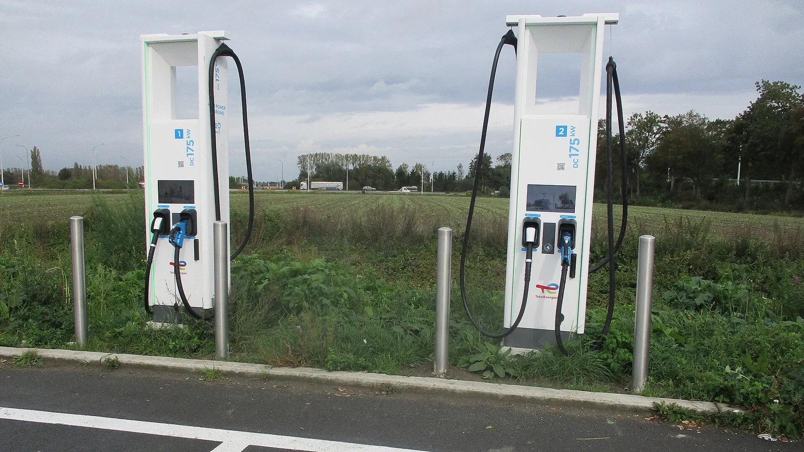 İki beyaz elektrikli araç şarj istasyonu, açık alanda yeşil çimle çevrili.