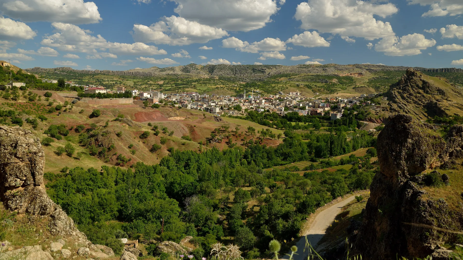 Yeşil vadideki tepelerin arasına kurulmuş küçük bir ilçe, üstünde bulutlu mavi gökyüzü