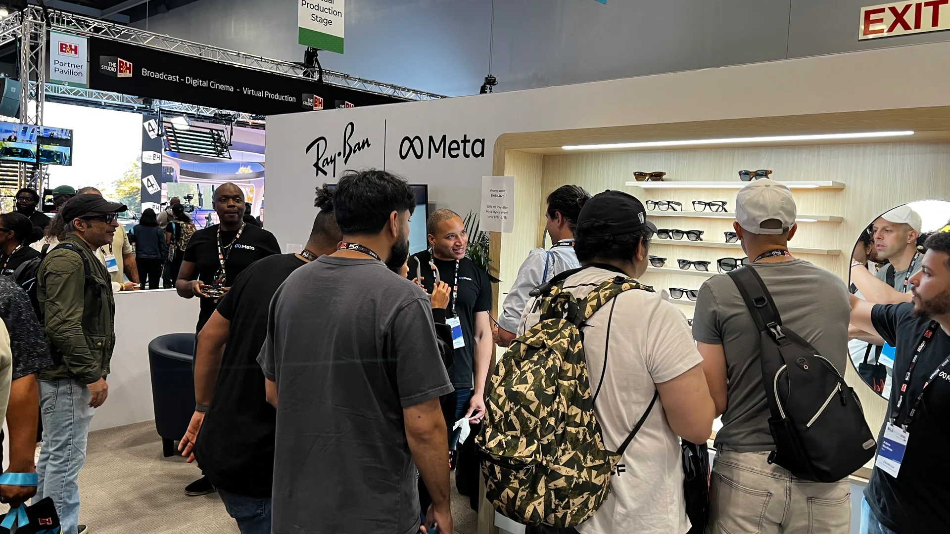 Ray-Ban ve Meta logolu fuarda insanlar akıllı gözlük standını inceliyor.