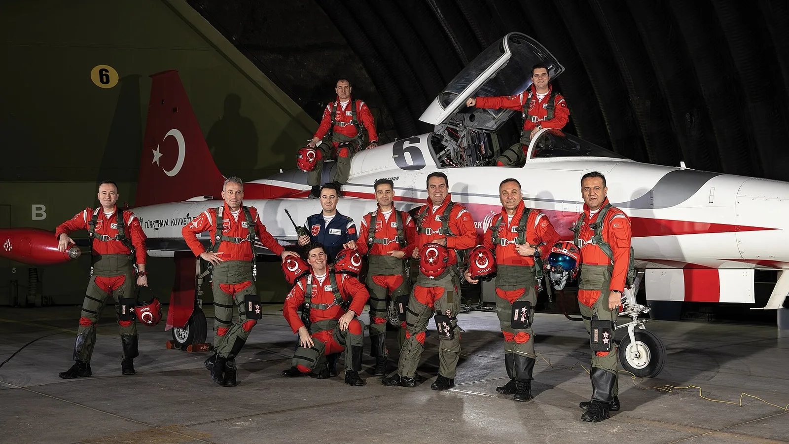Türk bayrağı taşıyan uçağın önünde, kırmızı-beyaz tören kıyafetli 11 pilot.